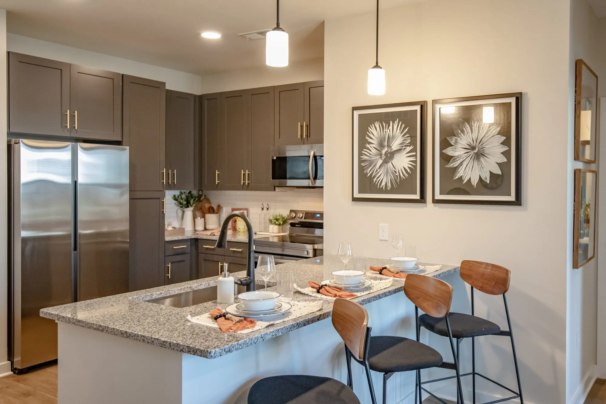 Multifamily model apartment kitchen with taupe shaker cabinets, a granite island set for two, wood barstools and pendants