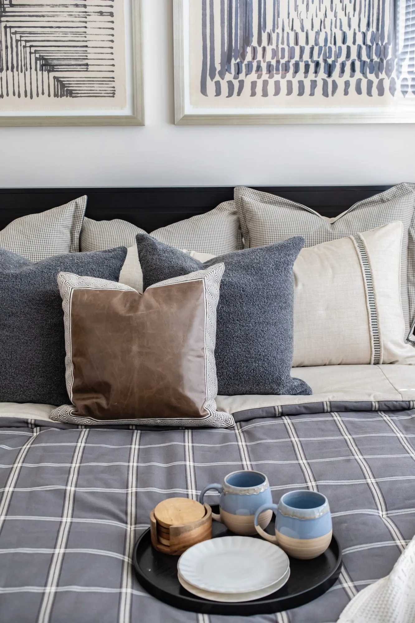 Multifamily apartment bedroom detail: grey, cream and leather pillows with a tray of mugs on a plaid duvet