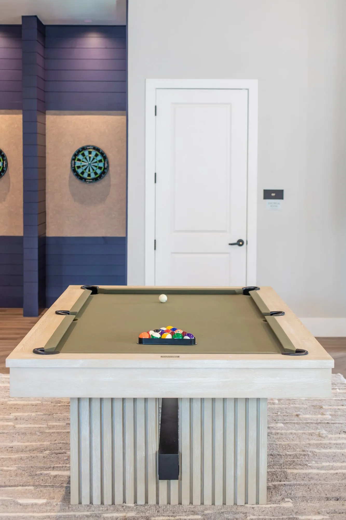 Multifamily amenity pool table with a fluted pale wood base before dart boards set into navy paneling