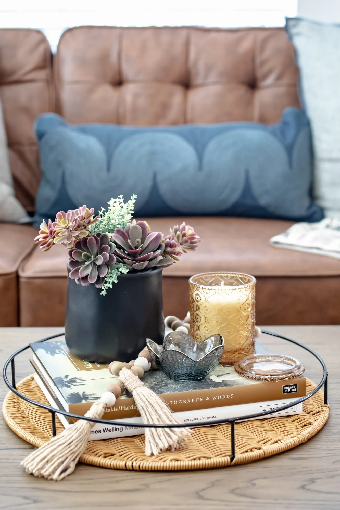 Multifamily interior detail: succulents in a black pot, a candle and books on a round rattan tray before a leather sofa