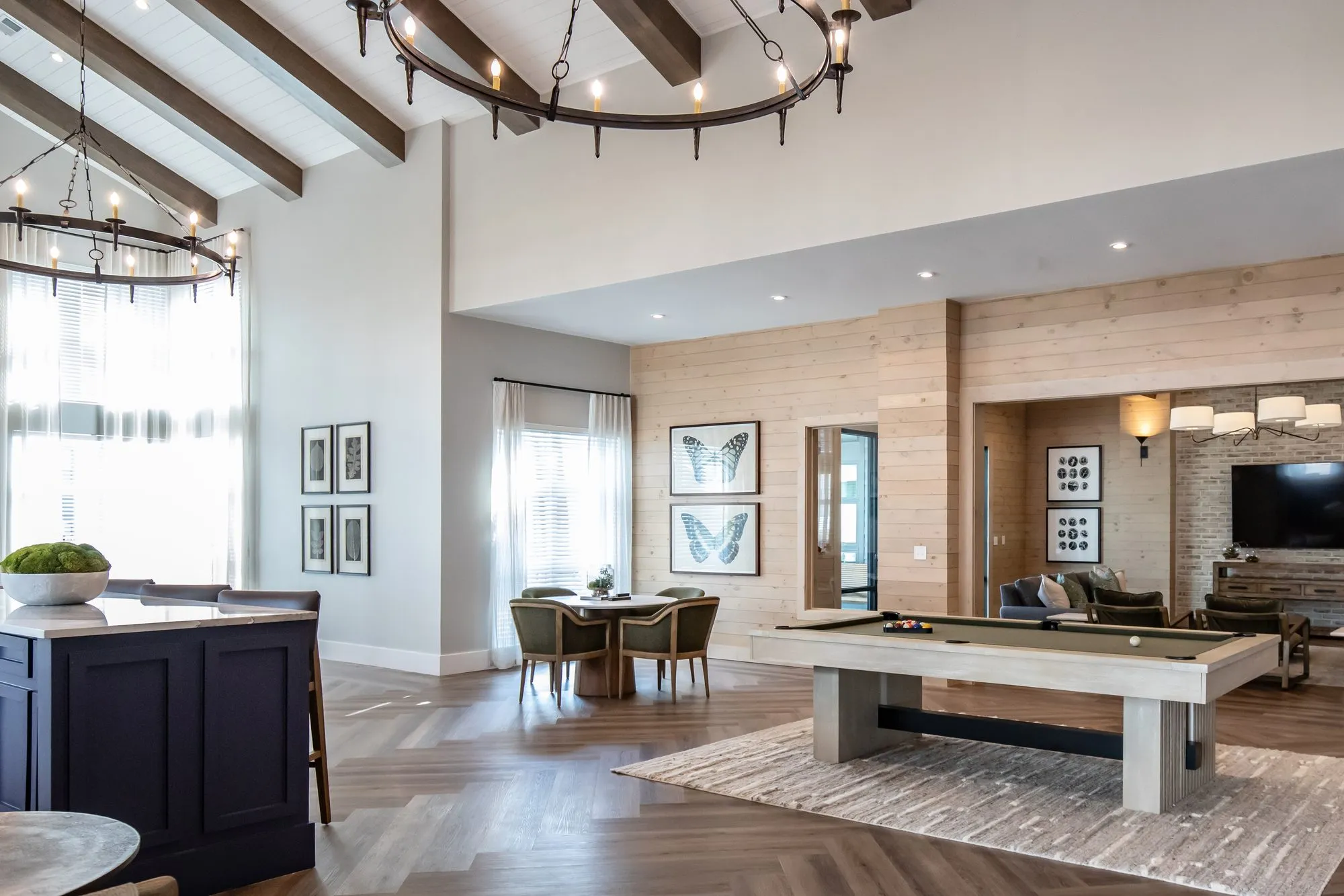 Multifamily amenity clubroom from the navy island, pool table and dining table beyond under iron ring chandeliers