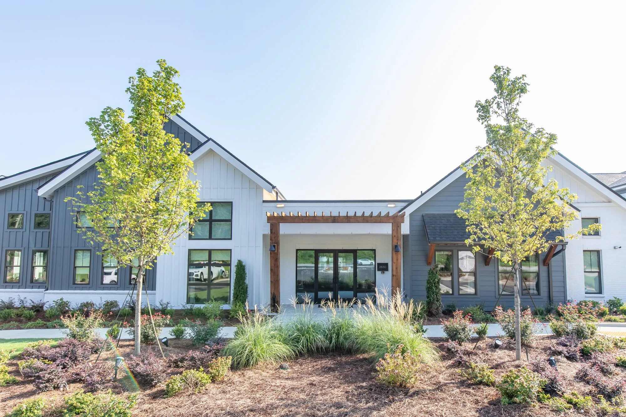 Multifamily community exterior: clubhouse with grey board and batten and white siding, gabled roofs and a timber pergola