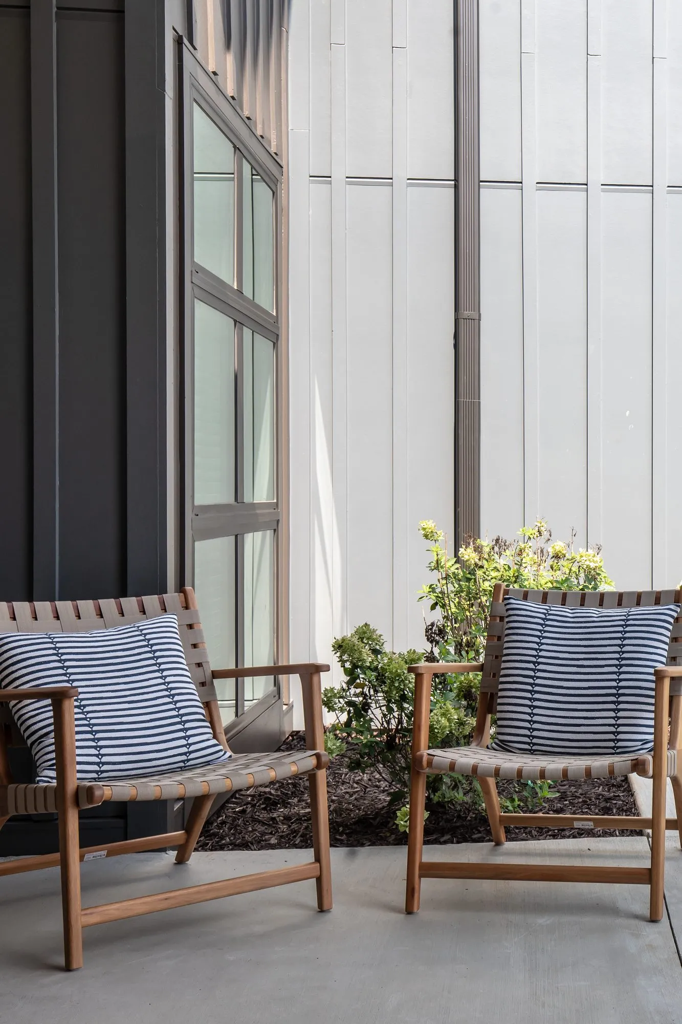 Multifamily covered patio with a pair of wood and woven strap lounge chairs with striped blue pillows