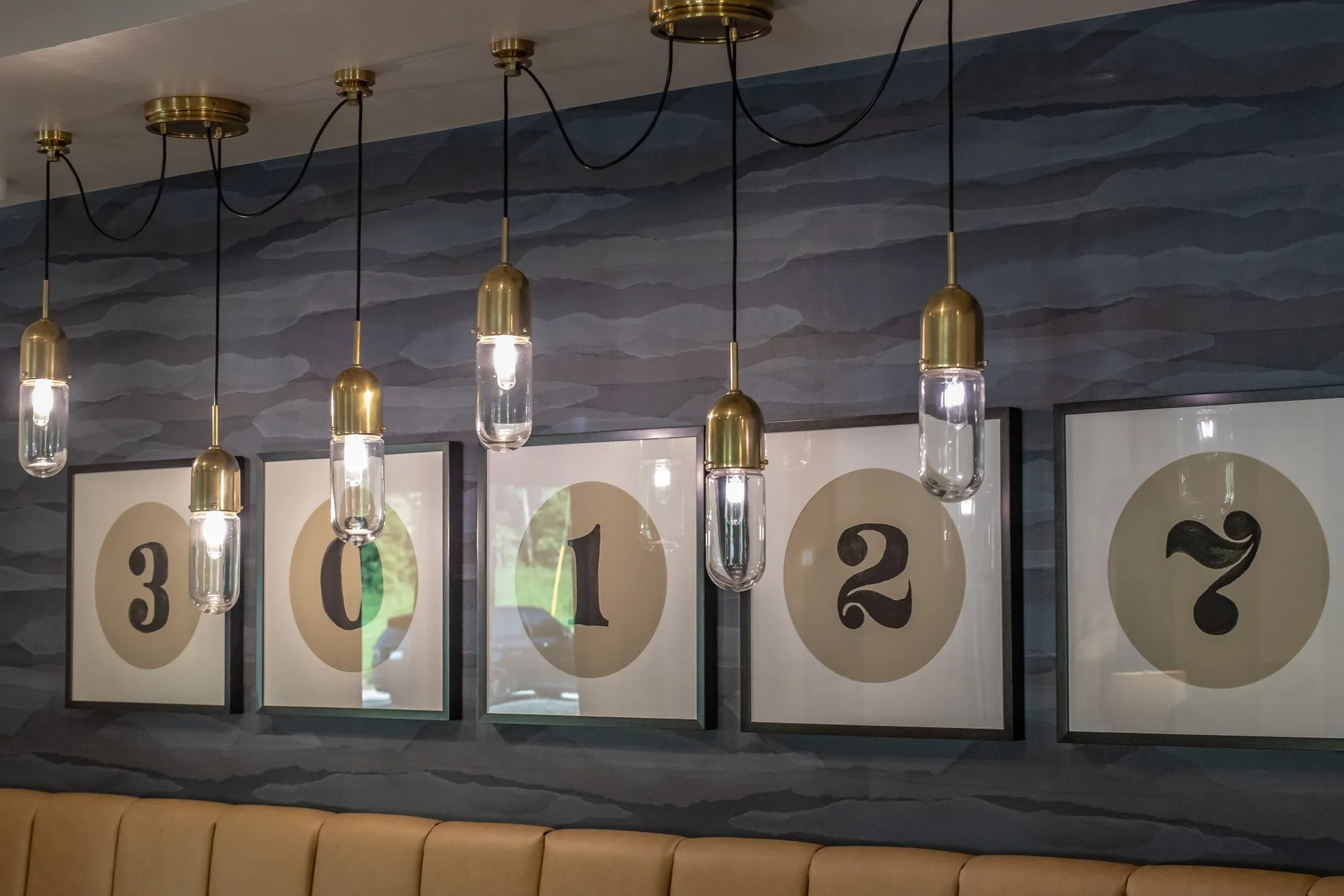 Multifamily interior detail: brass and glass pendants before numbered circle prints on a blue wave wallcovering