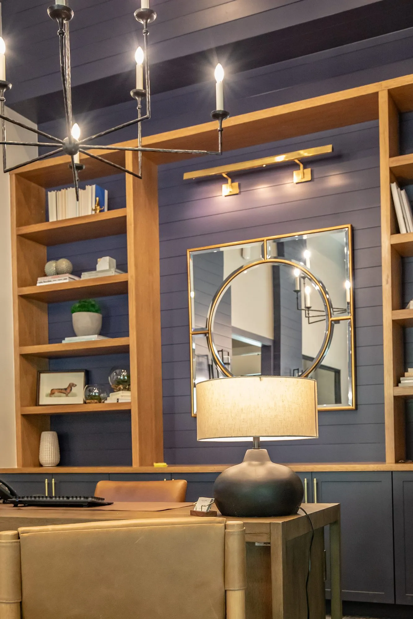 Multifamily interior detail: desk with a ceramic lamp before oak shelving and a round mirror on navy paneling