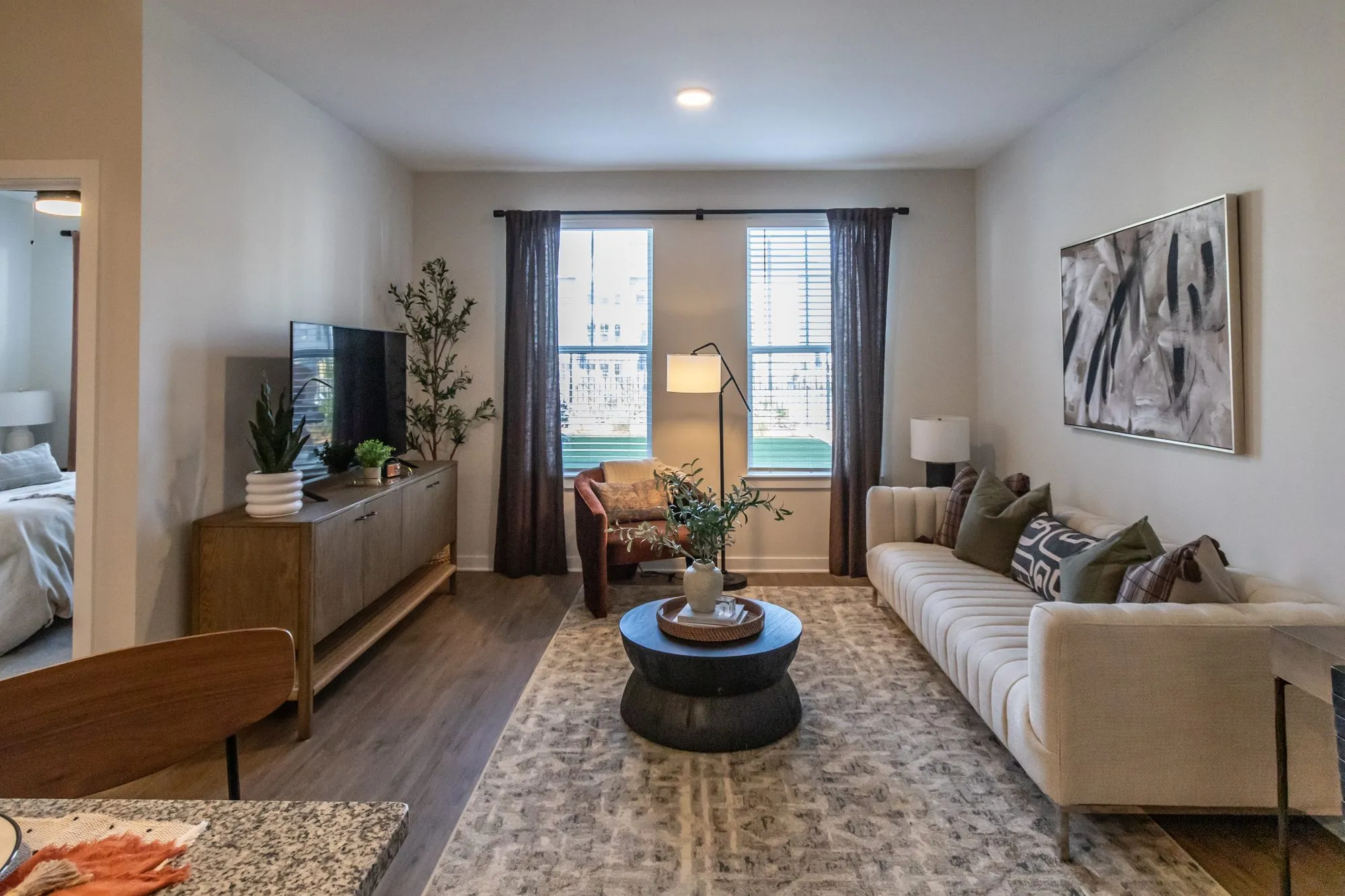 Multifamily model apartment living room with a cream sofa, black drum coffee table and wood media console on a patterned rug