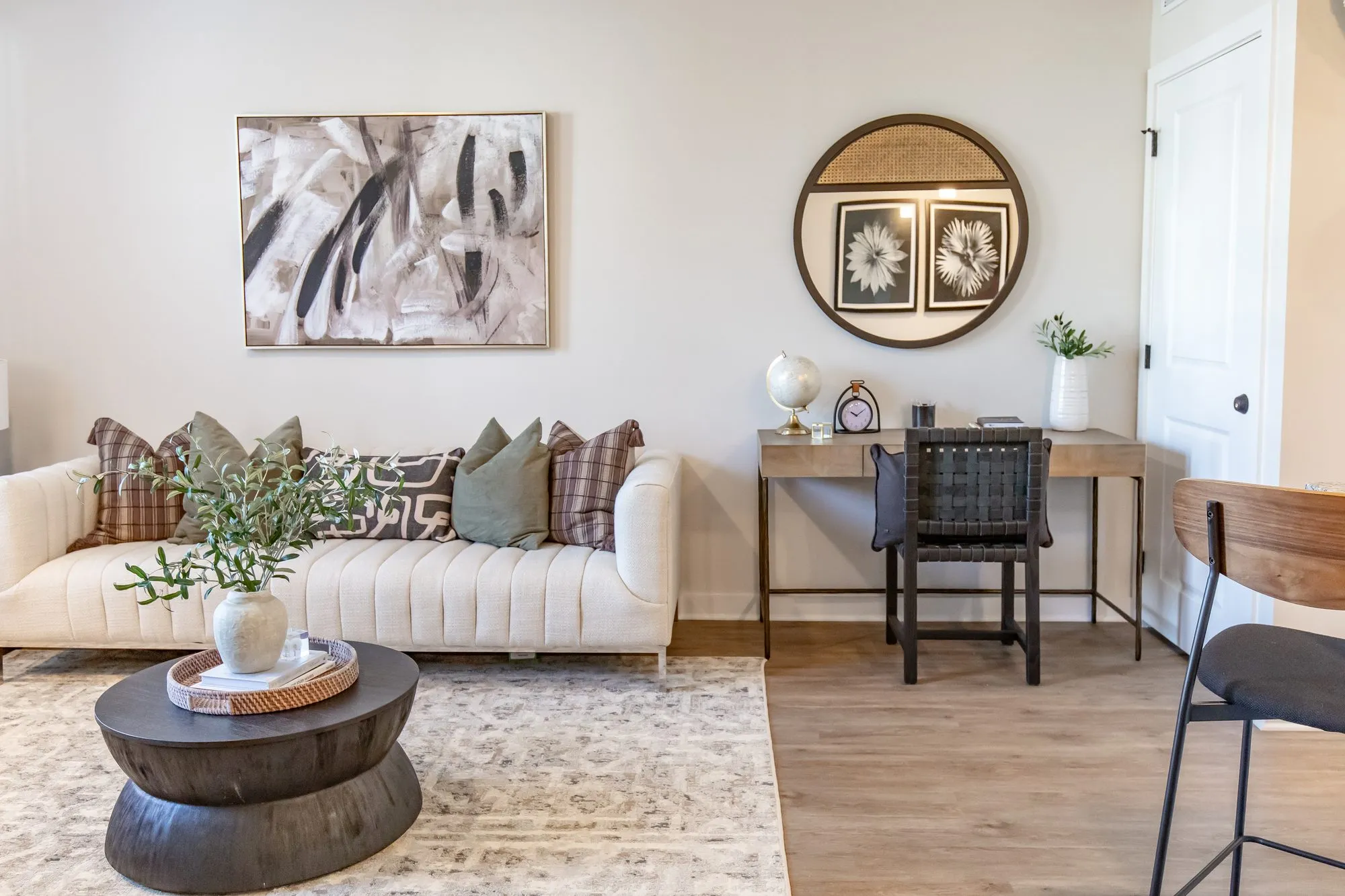 Multifamily apartment living room with a cream channel tufted sofa, black drum table and a small desk below a round mirror