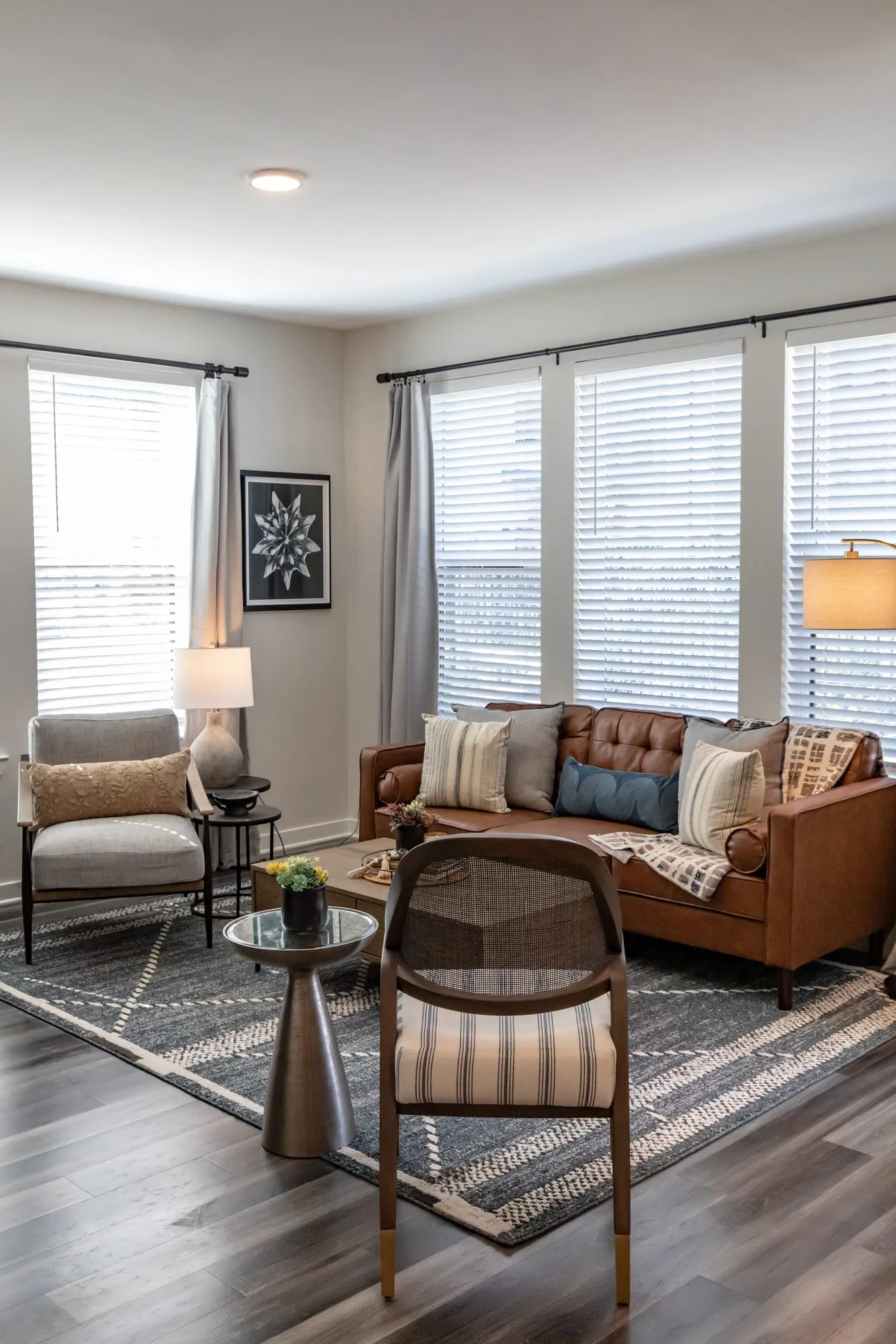 Multifamily model apartment living room with a cognac leather sofa, cane back chair and accent chair on a geometric rug