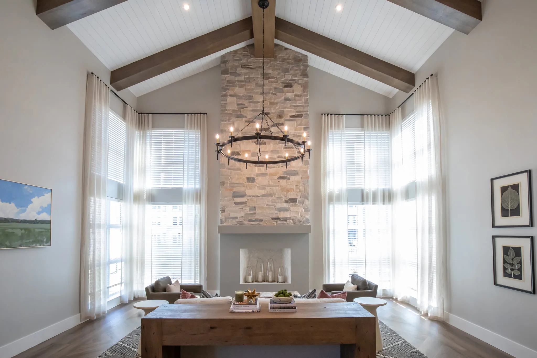 Multifamily amenity clubroom fireplace: stacked stone chimney rising into the beamed vaulted ceiling between sheer curtains