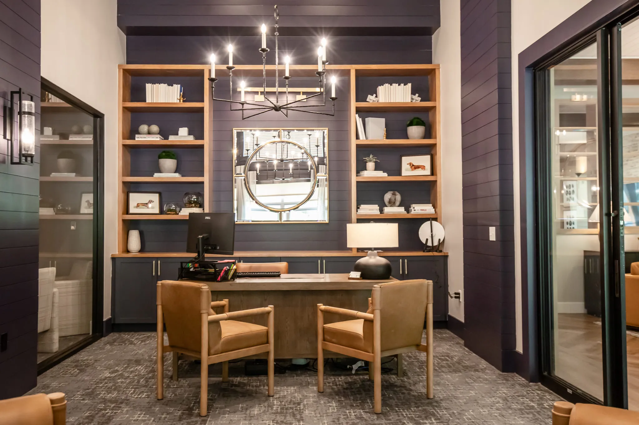 Multifamily amenity office with two leather chairs before a wood desk and monitor, built-in shelving on aubergine paneling