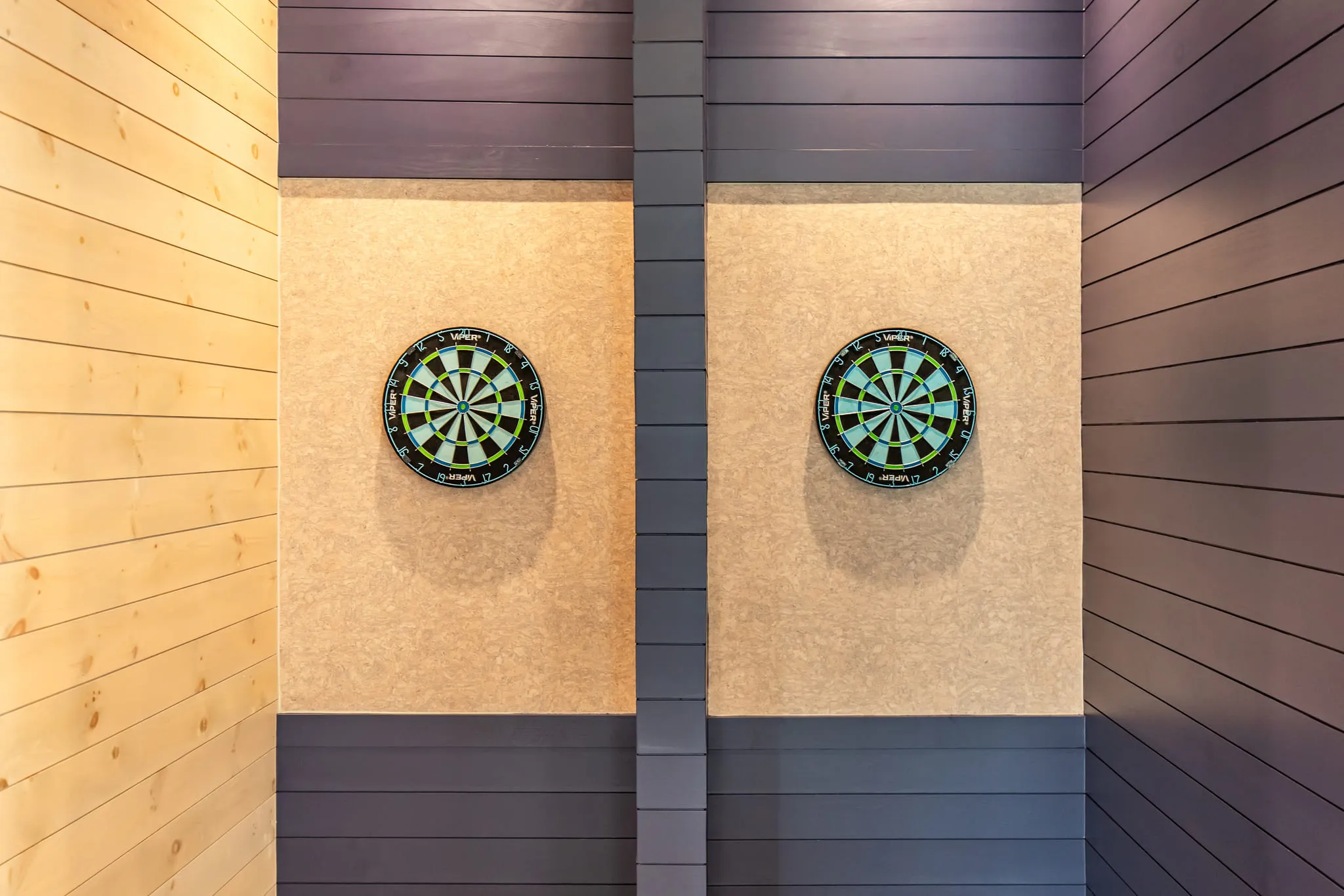Multifamily amenity dart boards: two boards on light backing panels set into navy and natural tongue-and-groove paneling