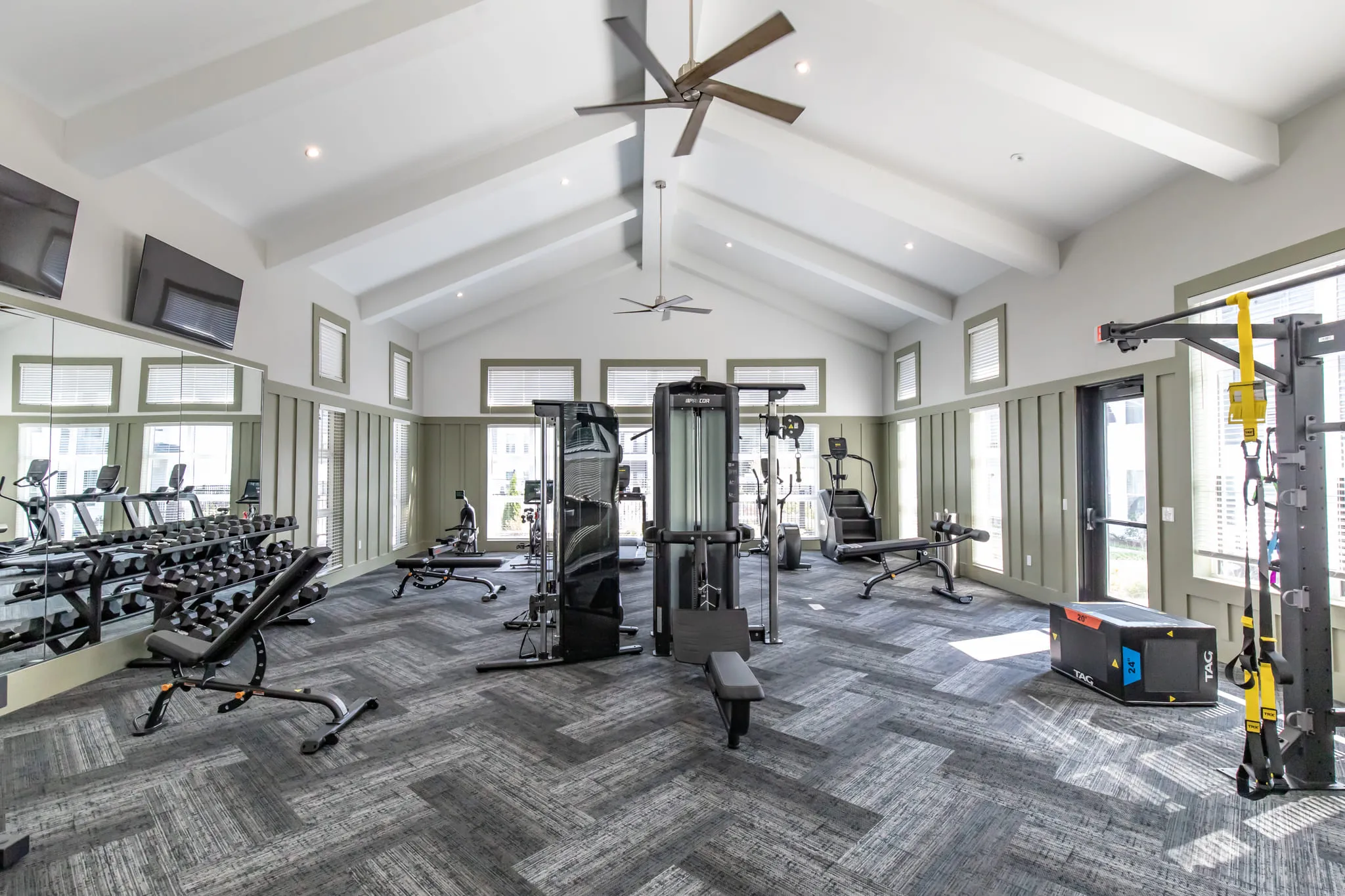 Multifamily amenity fitness center with weight machines and free weights under a vaulted ceiling with exposed beams