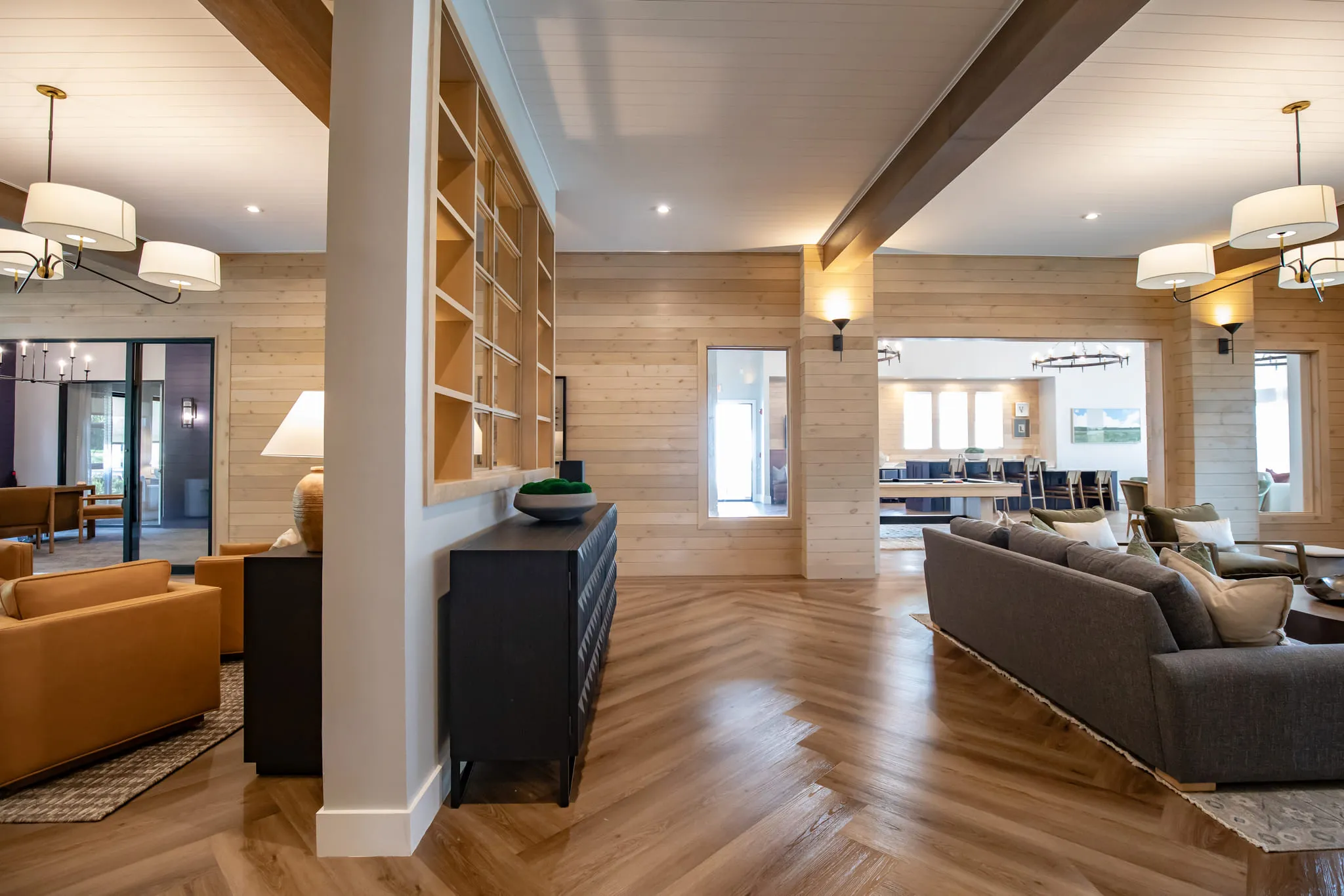 Multifamily amenity lounge with open built-in shelving above a black console between leather armchairs and a grey sofa