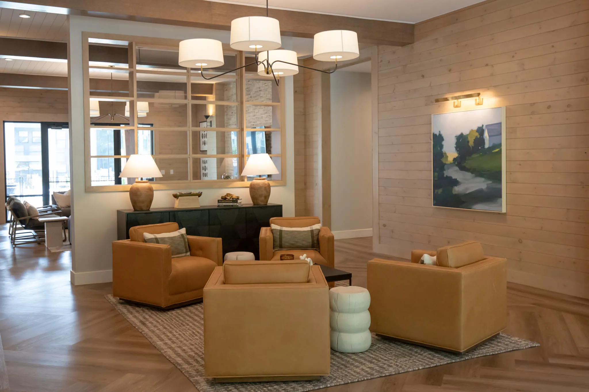 Multifamily amenity lounge with tan leather armchairs and drum pendants against wood plank walls