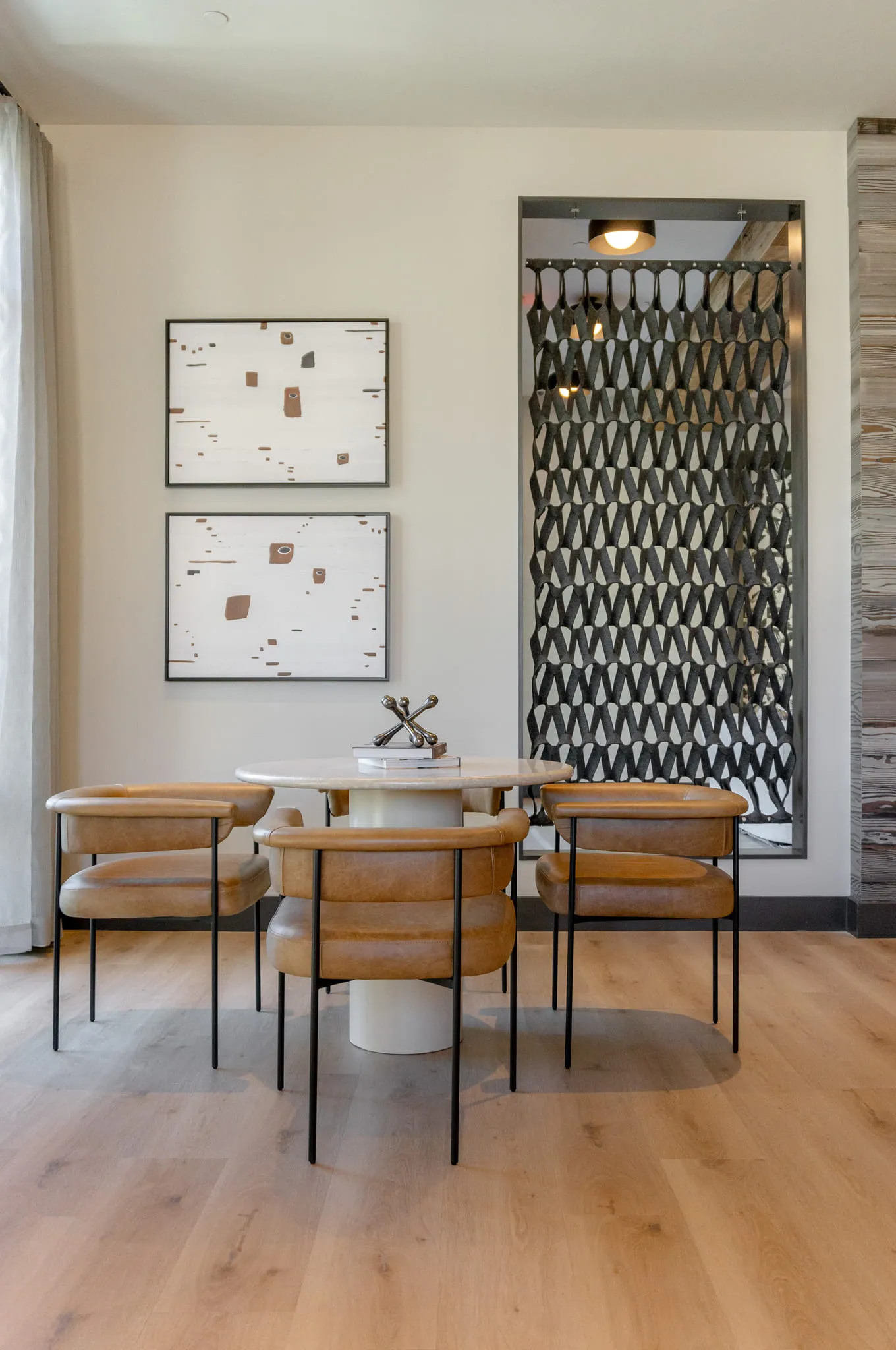 Multifamily dining nook with a round stone table and tan leather chairs beside a woven acoustic panel