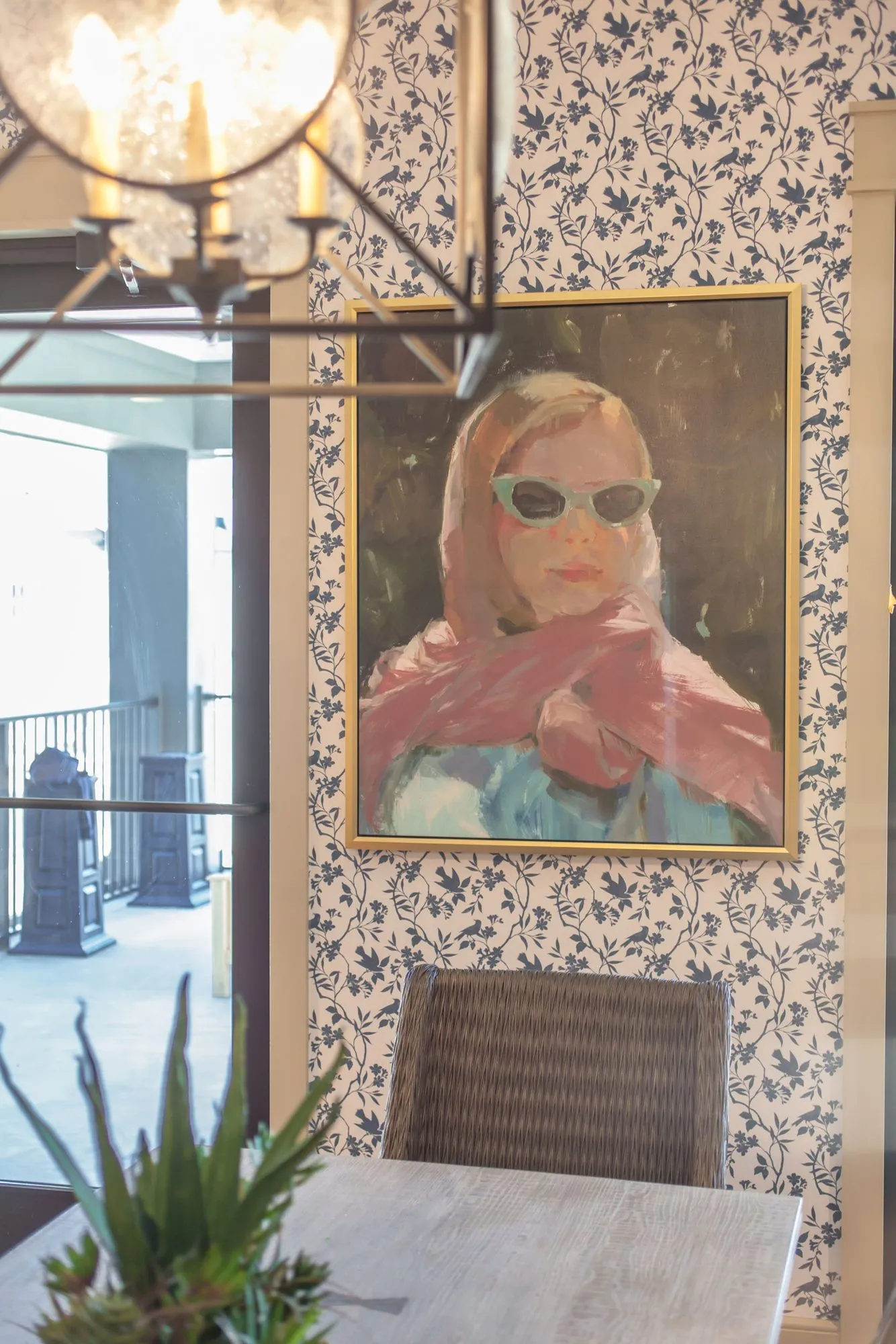 Senior living interior detail: painting of a woman in sunglasses and a pink scarf on blue floral wallpaper