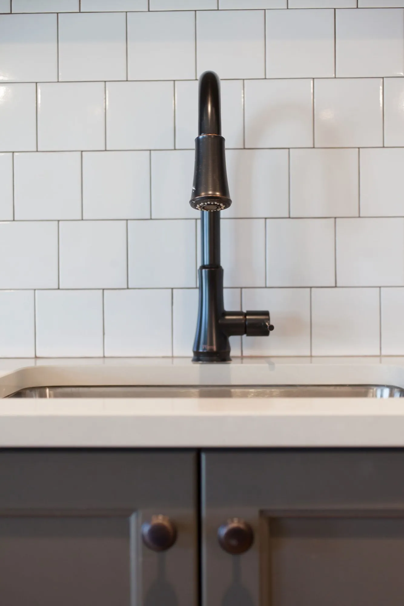 Senior living interior detail: black faucet over a sink with white subway tile and charcoal cabinetry