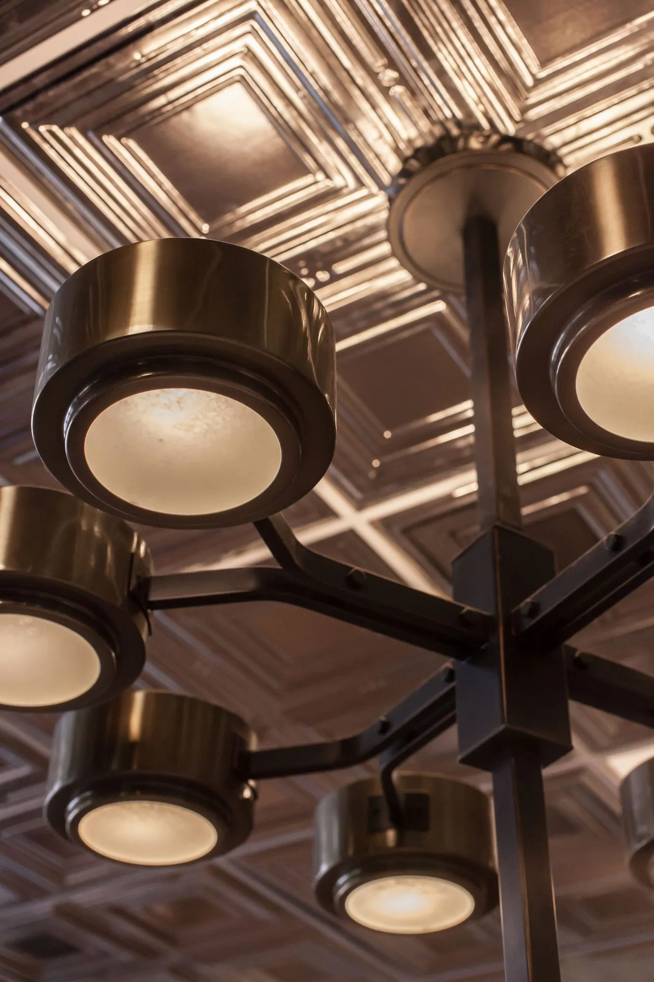Senior living interior detail: looking up at a bronze multi-arm light fixture with round shades against a pressed tin ceiling
