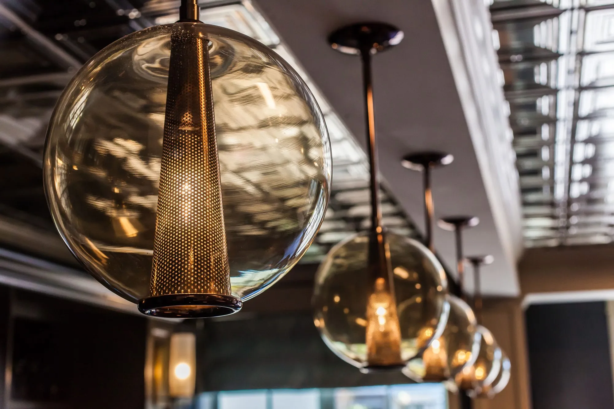 Senior living bar detail: clear glass globe pendants with brass mesh cones hanging in a row over the bar