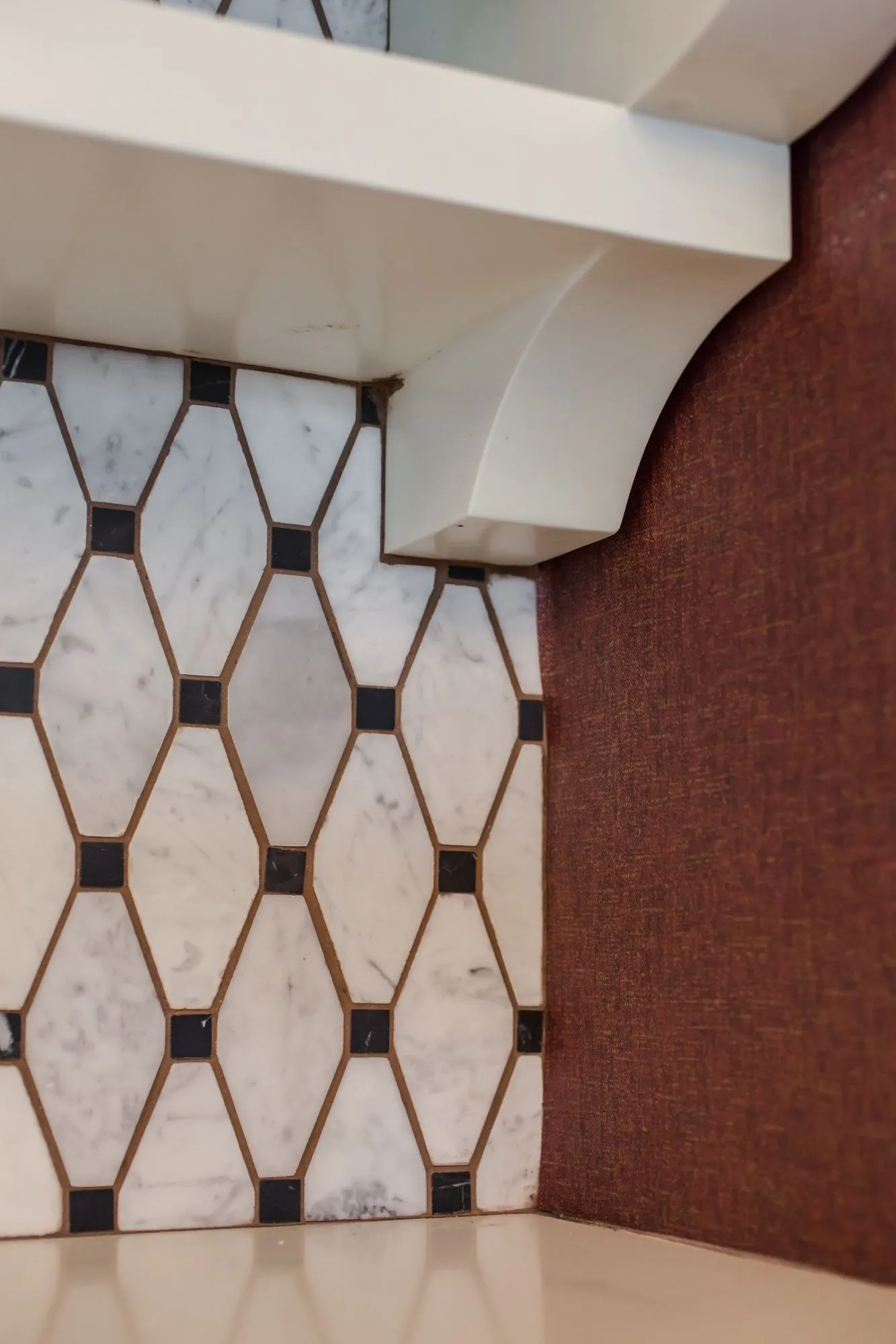 Senior living interior detail: white marble elongated hexagon tile with black dots below a white corbel and red textured wall