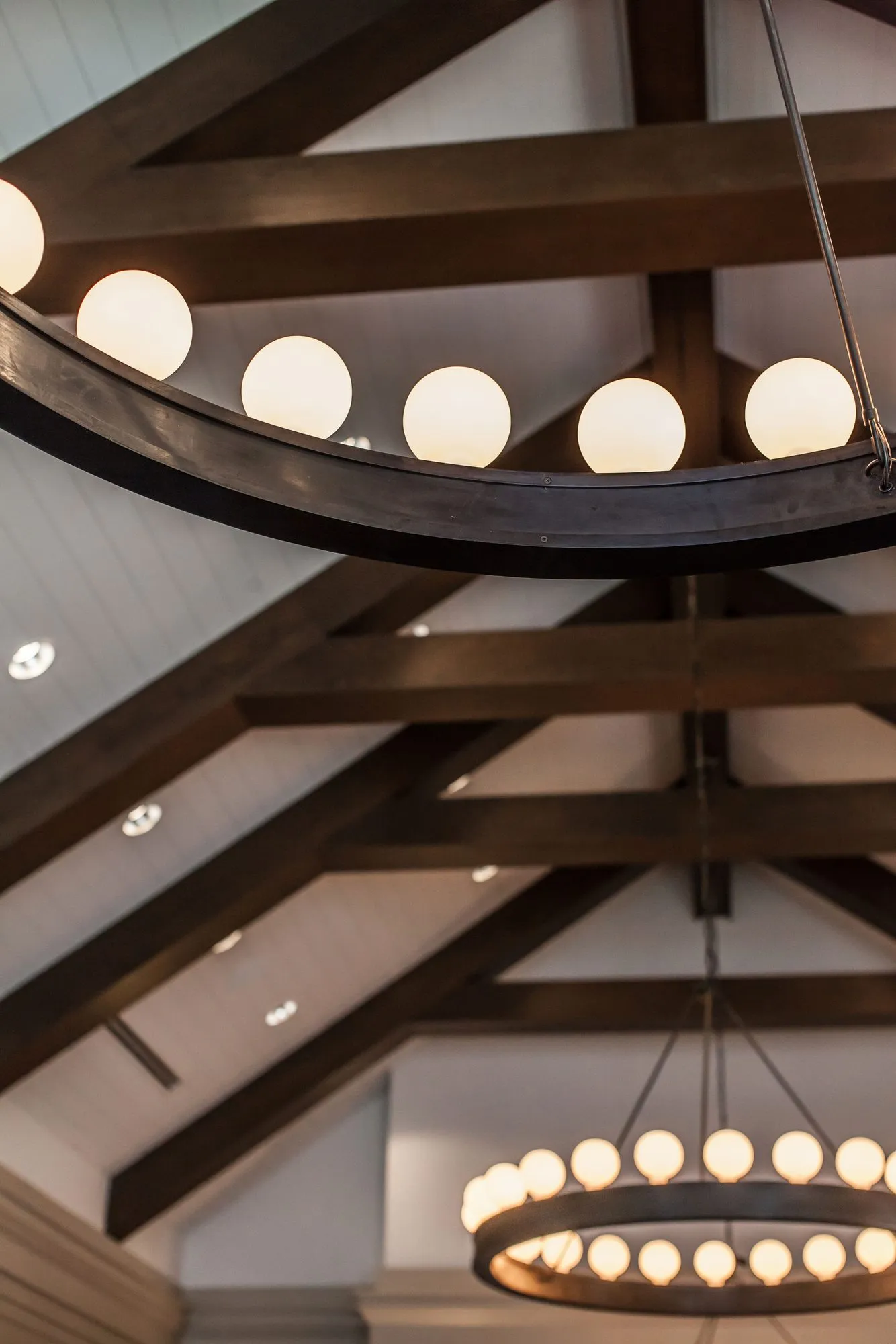 Senior living interior detail: two ring chandeliers with white globe lights between dark stained timber trusses