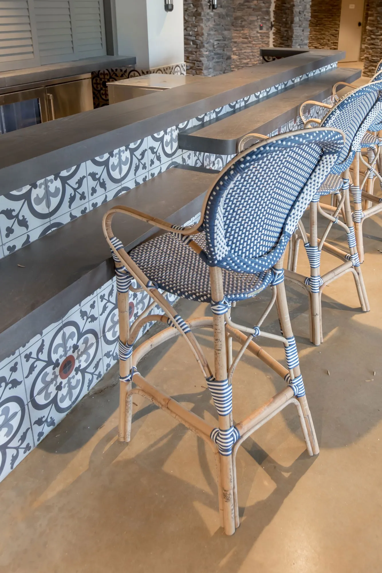 Senior living interior detail: rattan bistro barstools with blue and white woven seats at a counter faced in cement tile