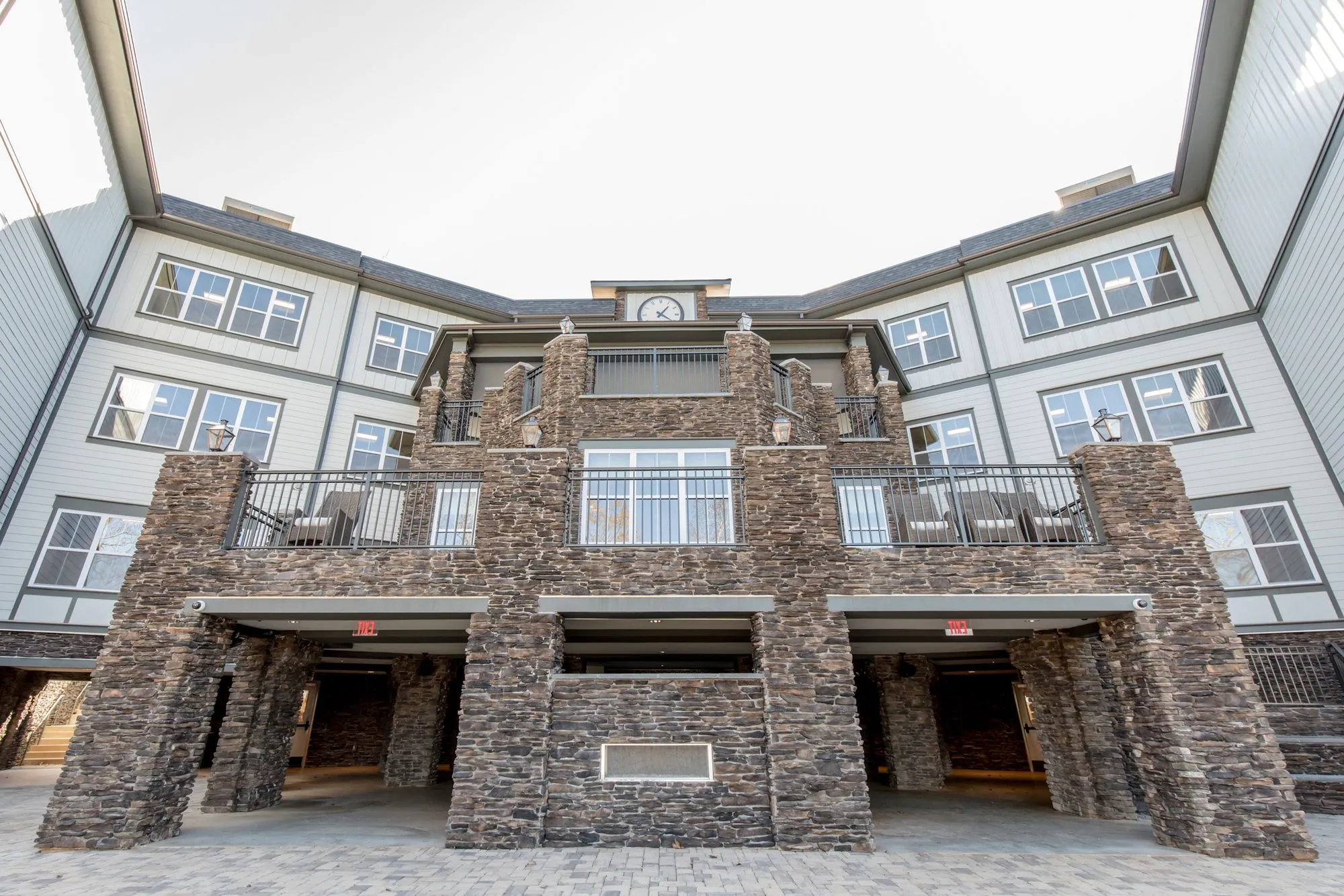 Senior living community exterior: rear facade with stacked stone walls and balconies between grey sided wings to a clock