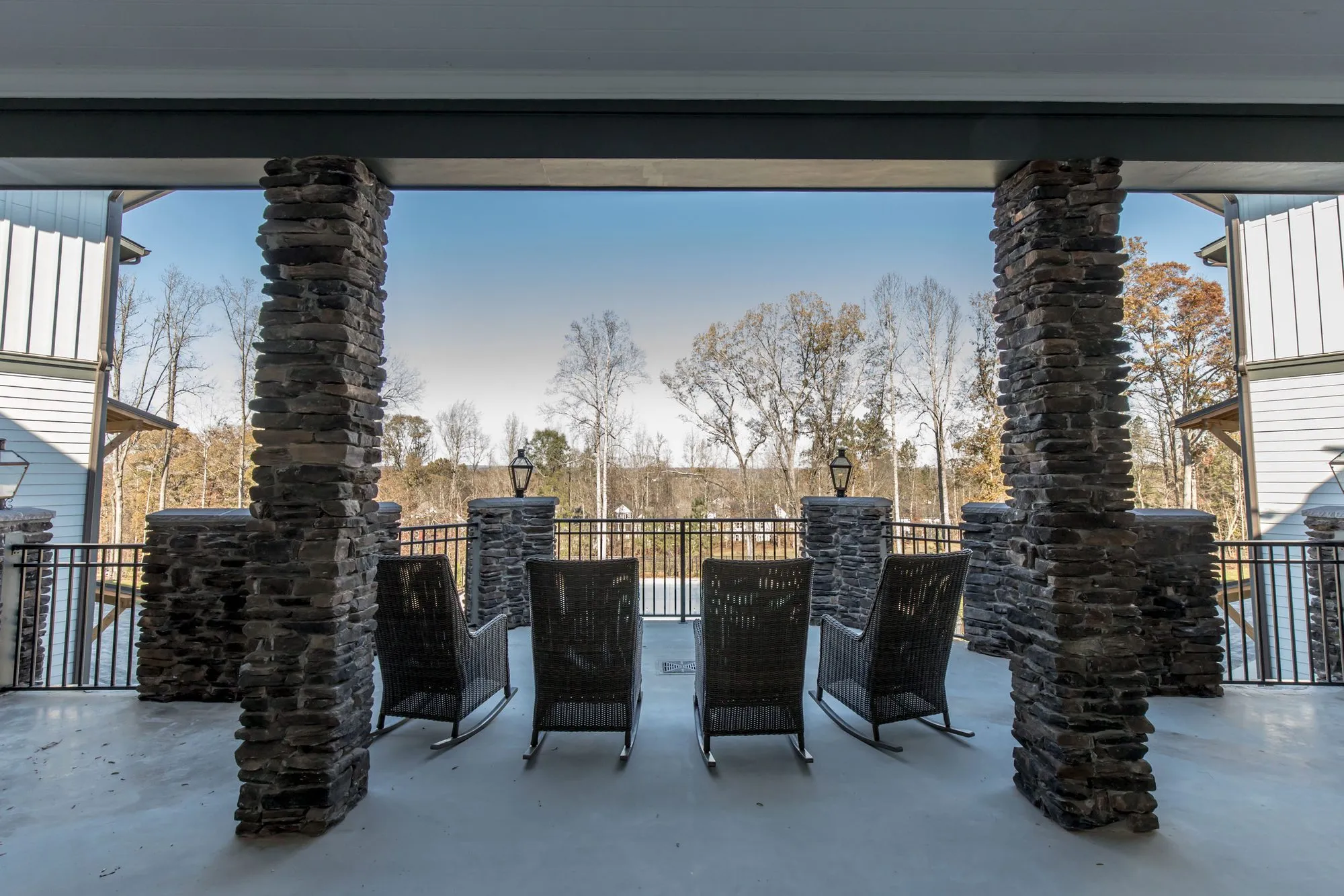 Senior living covered porch with rocking chairs between stacked stone columns, looking out over a railing to trees