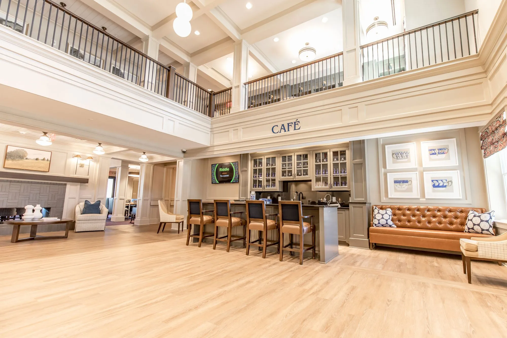 Senior living two storey cafe and lounge with a gallery balcony, barstools at the counter and a cognac tufted sofa
