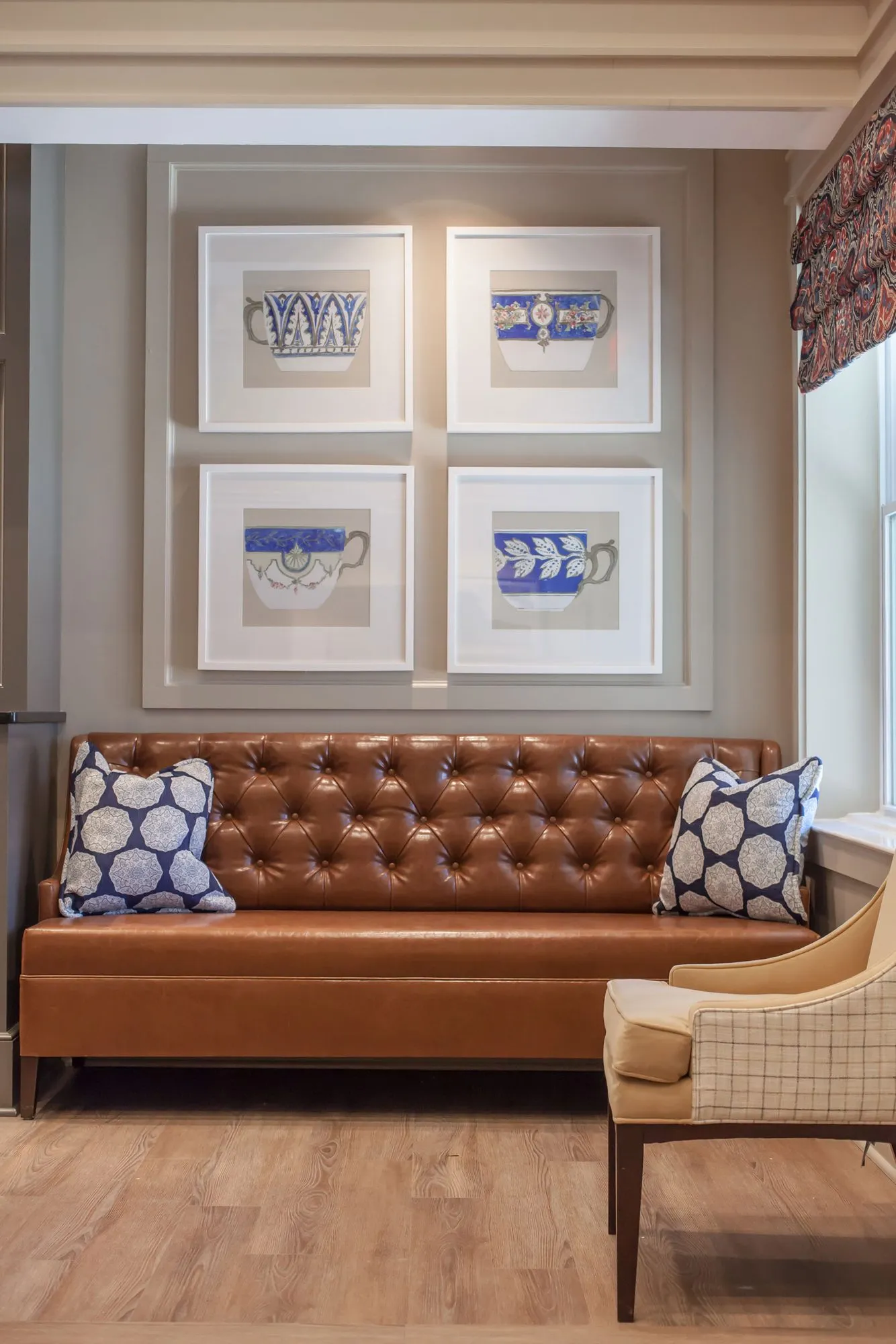 Senior living interior detail: cognac tufted leather sofa with blue pillows below four framed teacup prints