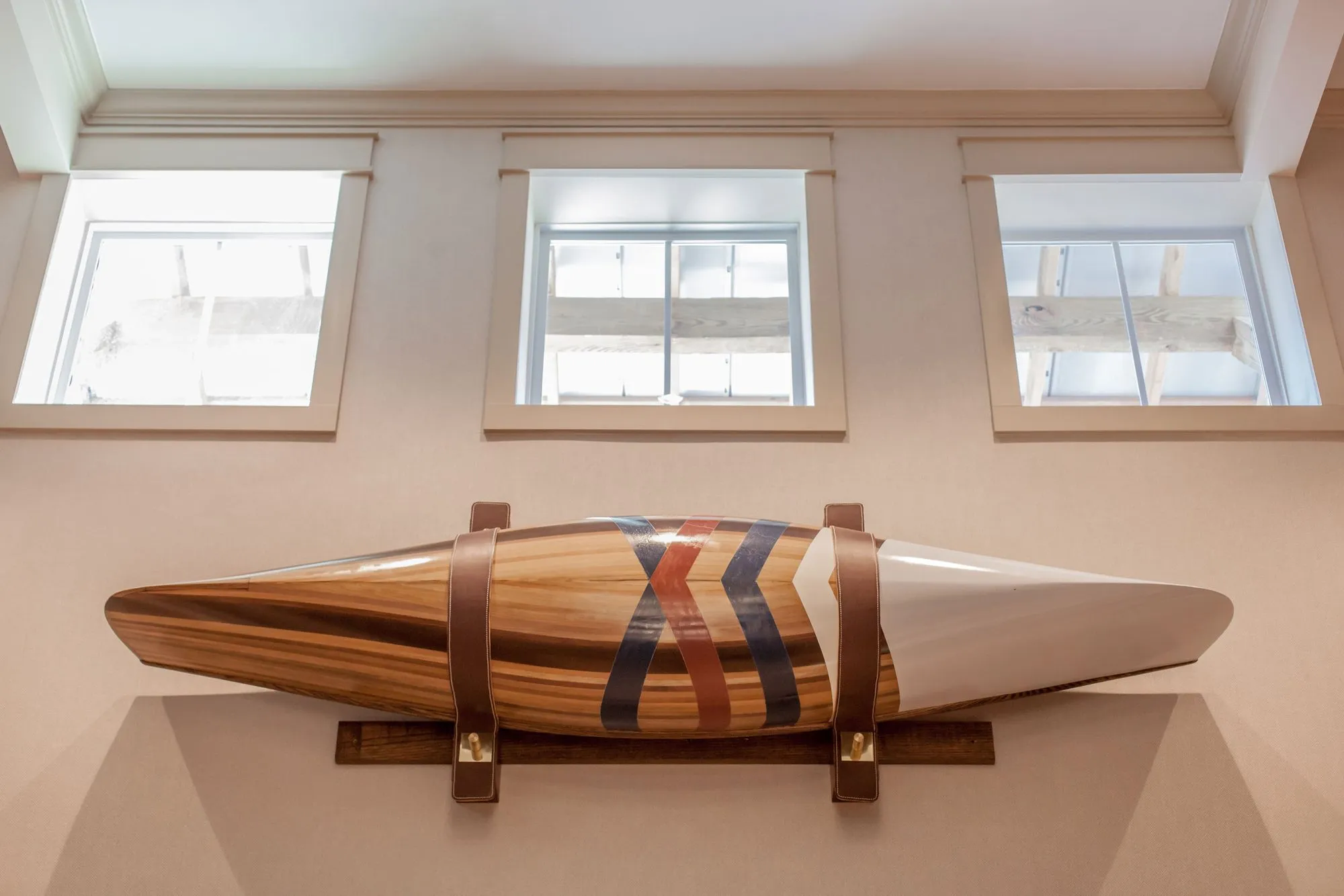 Senior living interior detail: striped wooden boat hull mounted on leather straps below three clerestory windows