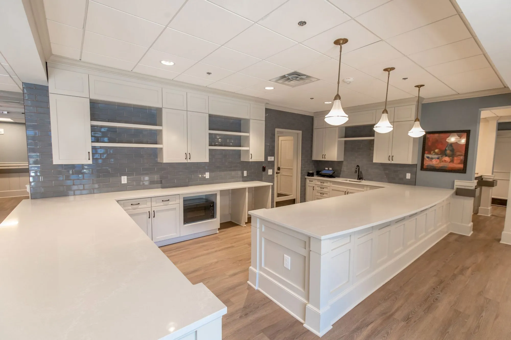 Senior living kitchen with white cabinets, quartz counters, a large peninsula, blue grey subway tile and glass pendants