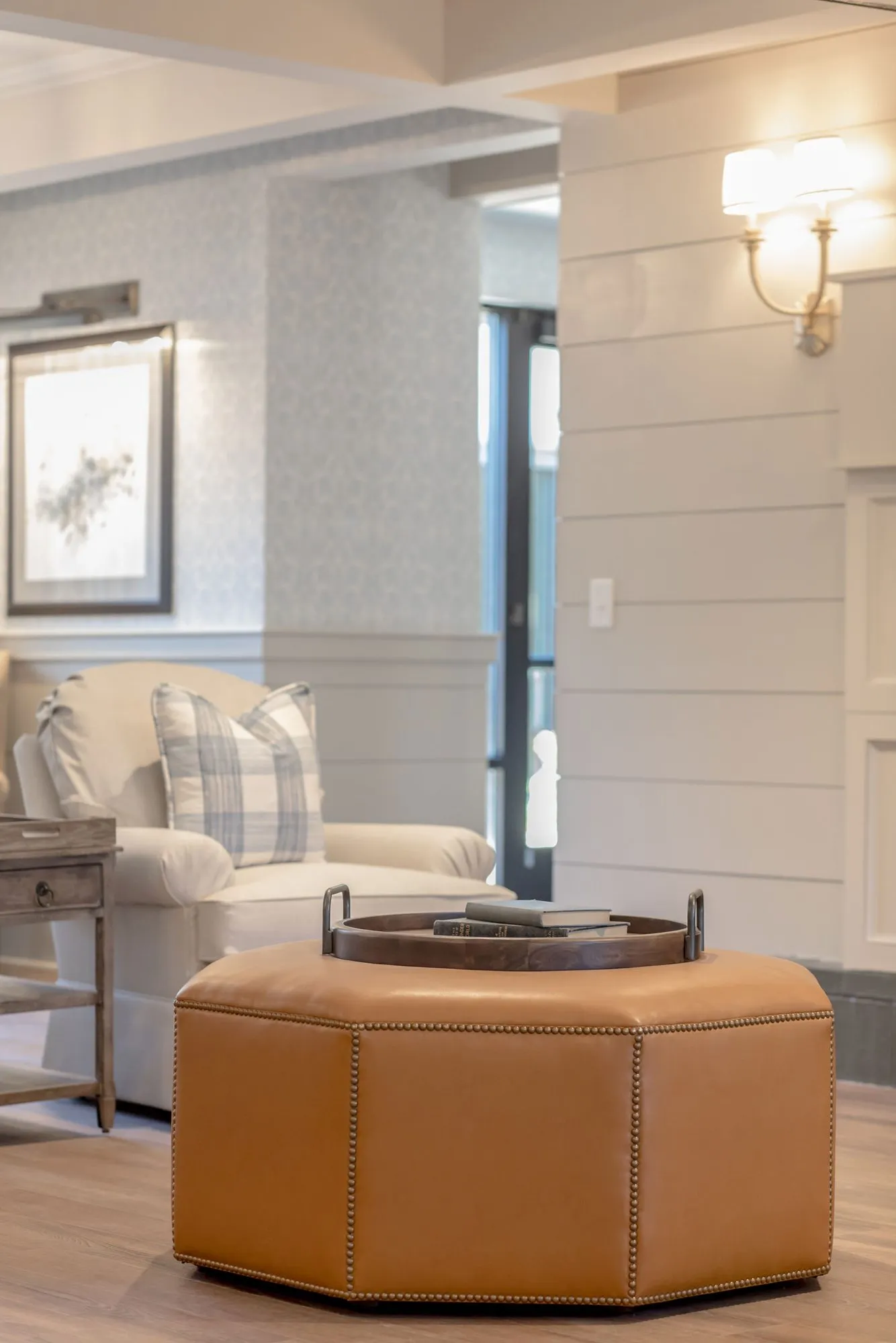 Senior living interior detail: cognac leather hexagonal ottoman before a cream club chair, framed floral print beyond