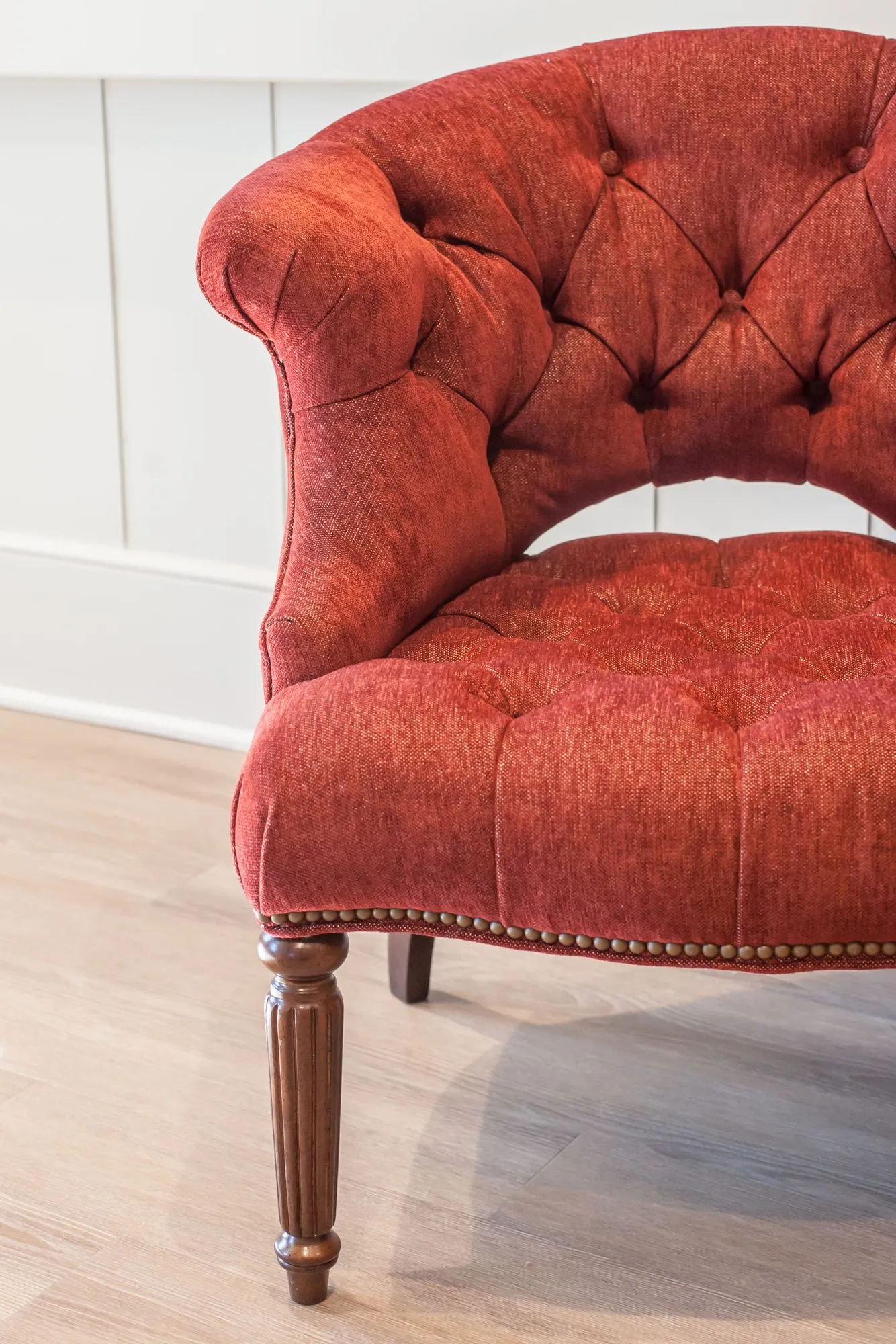 Senior living interior detail: red tufted slipper chair with nailhead trim and turned wood legs
