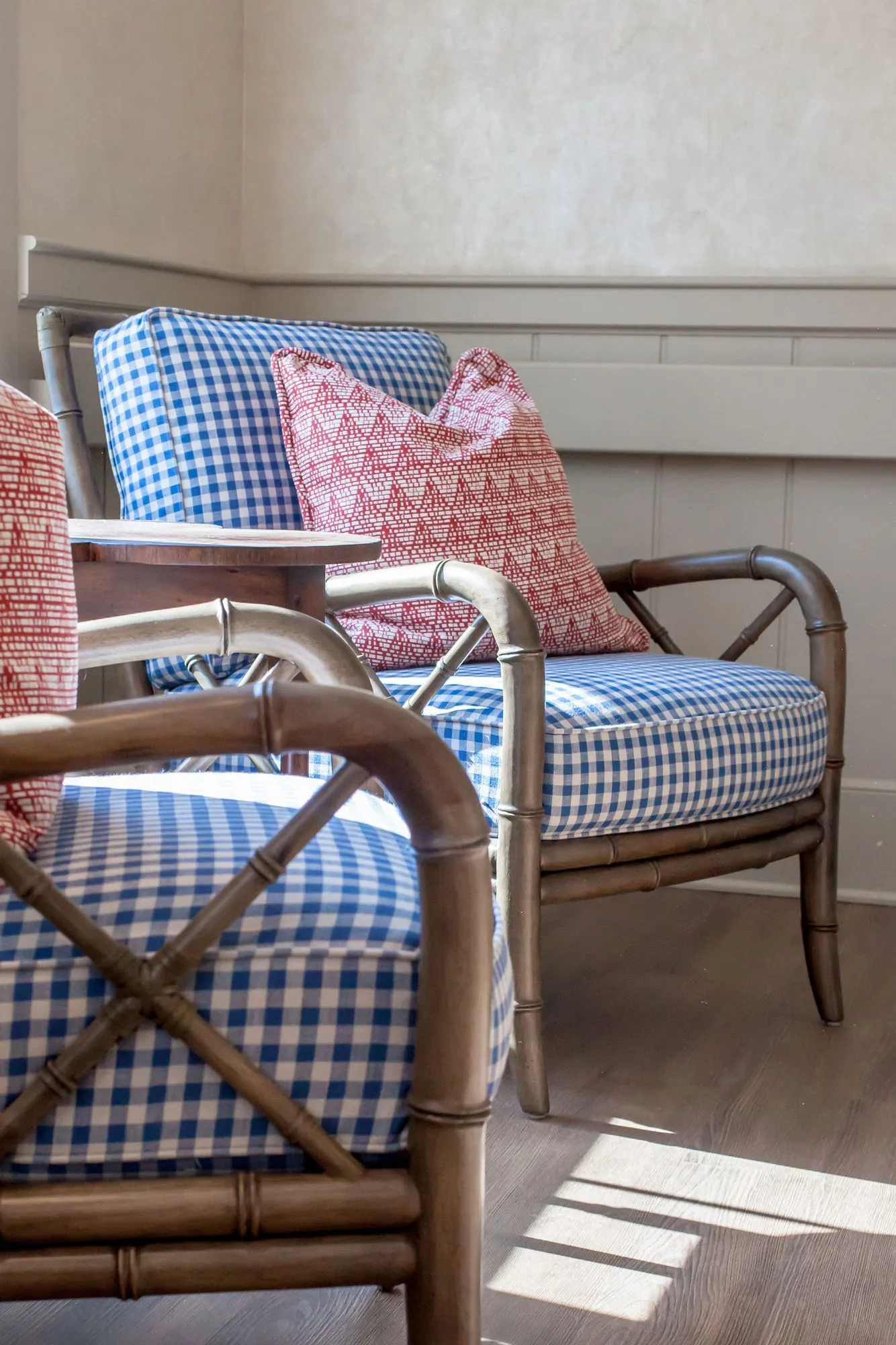 Senior living interior detail: faux bamboo armchairs in blue gingham with red patterned pillows by a window