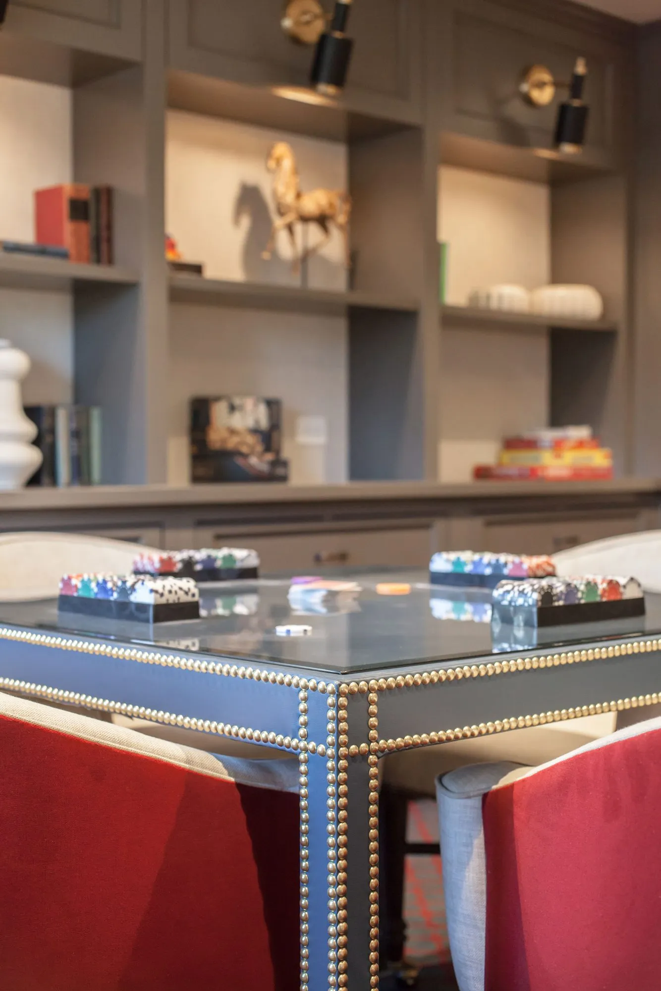 Senior living interior detail: nailhead trimmed glass top game table with chip racks, grey built-in shelves behind