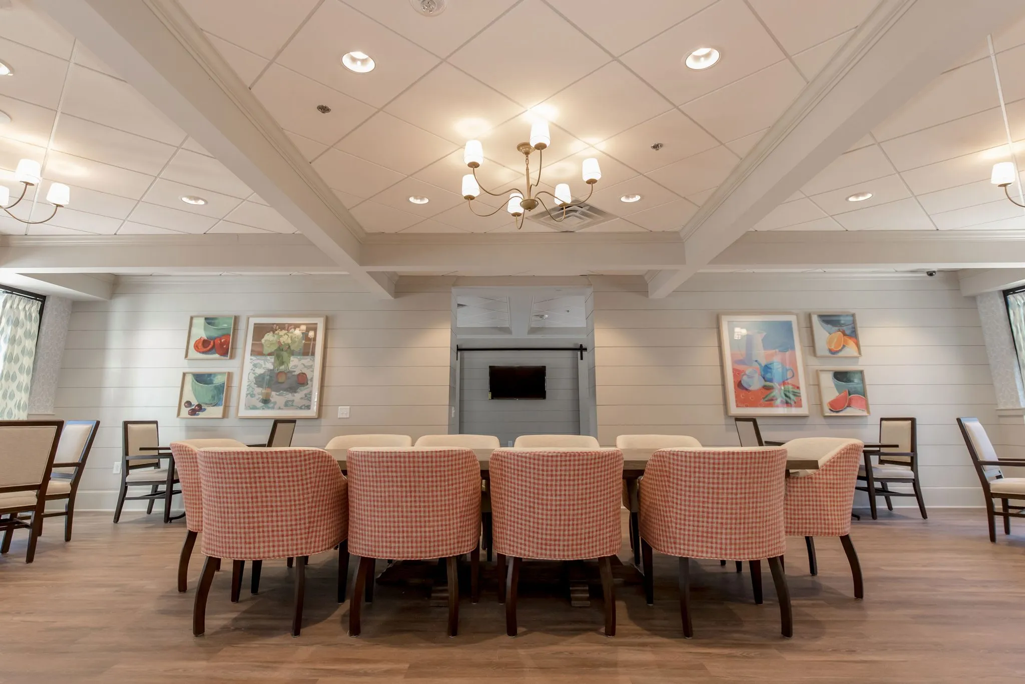 Senior living memory care dining room with coral checked chairs at long tables under a coffered ceiling