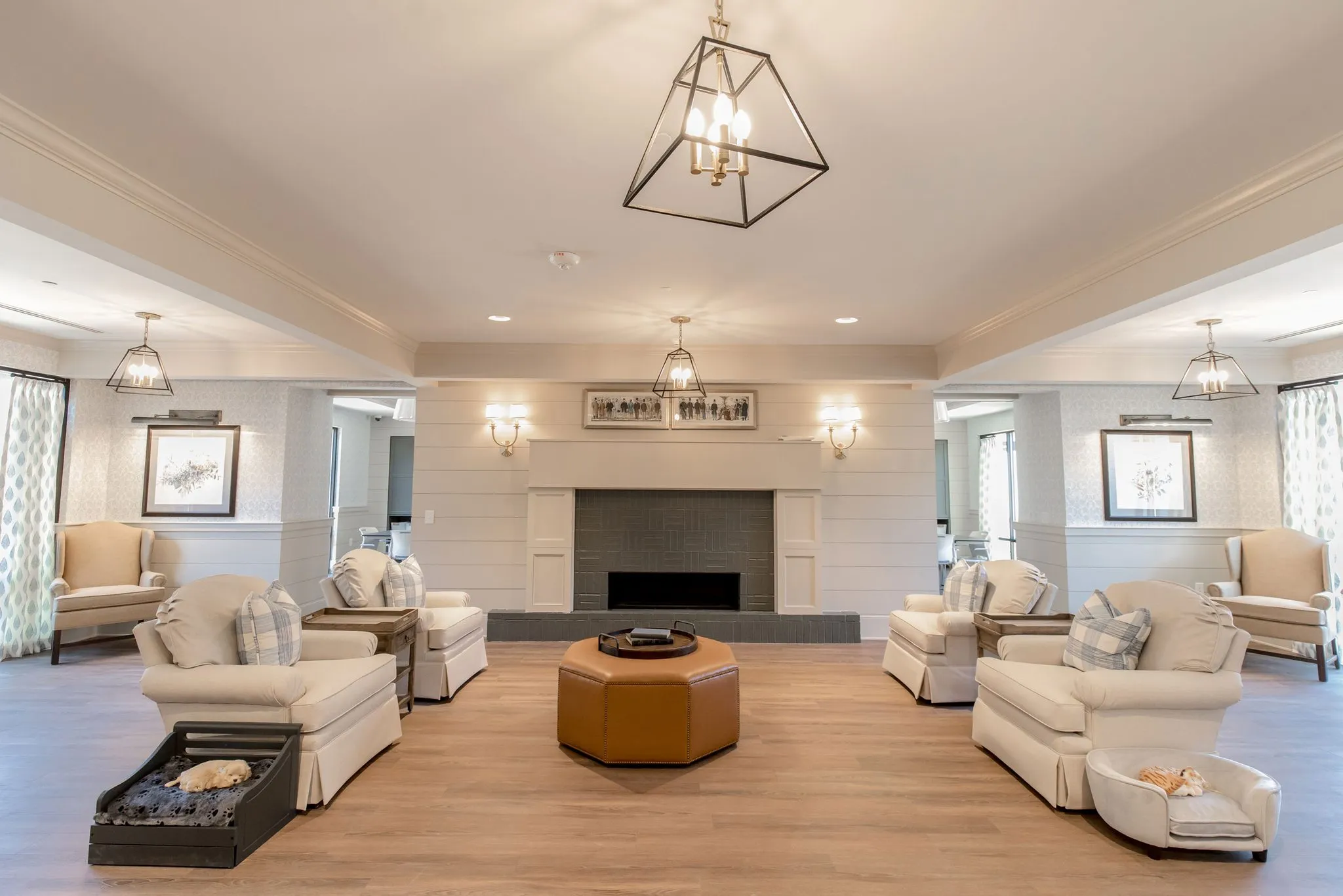 Senior living memory care living room with cream club chairs around an octagonal leather ottoman before the fireplace