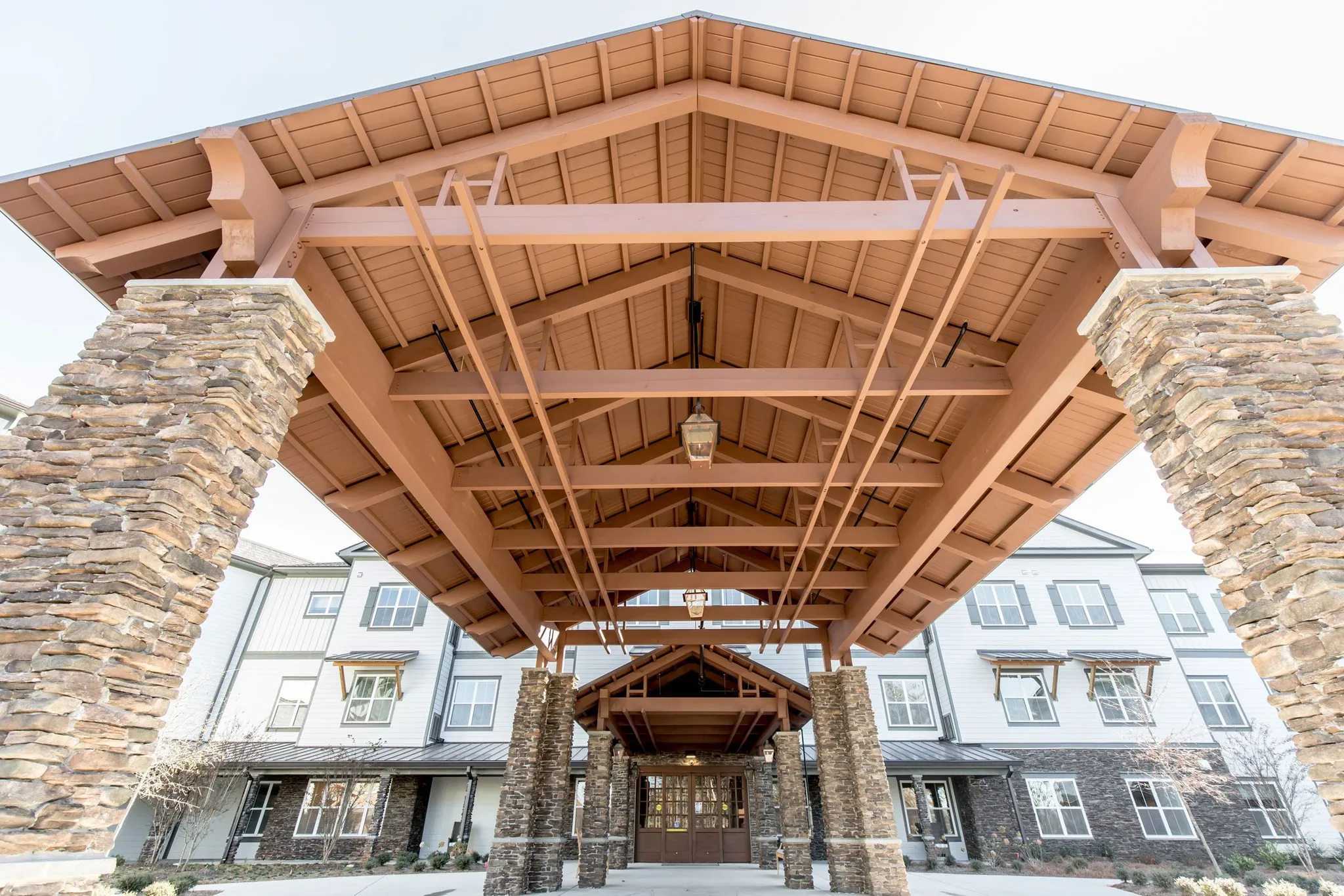 Senior living community exterior: arrival canopy with heavy timber trusses carried on stacked stone columns