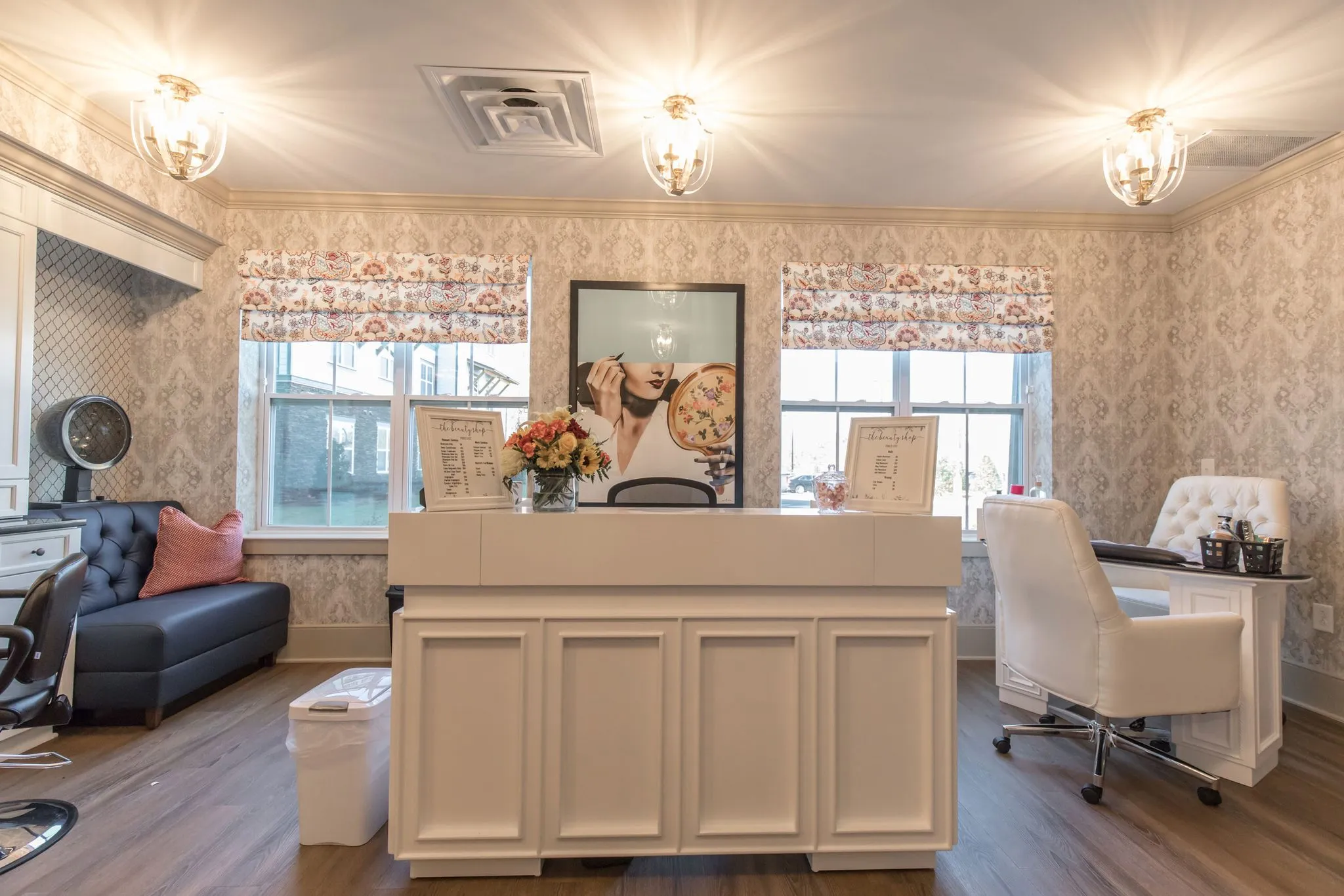 Senior living salon with a cream reception counter, a white tufted salon chair and a hood dryer on damask wallpaper