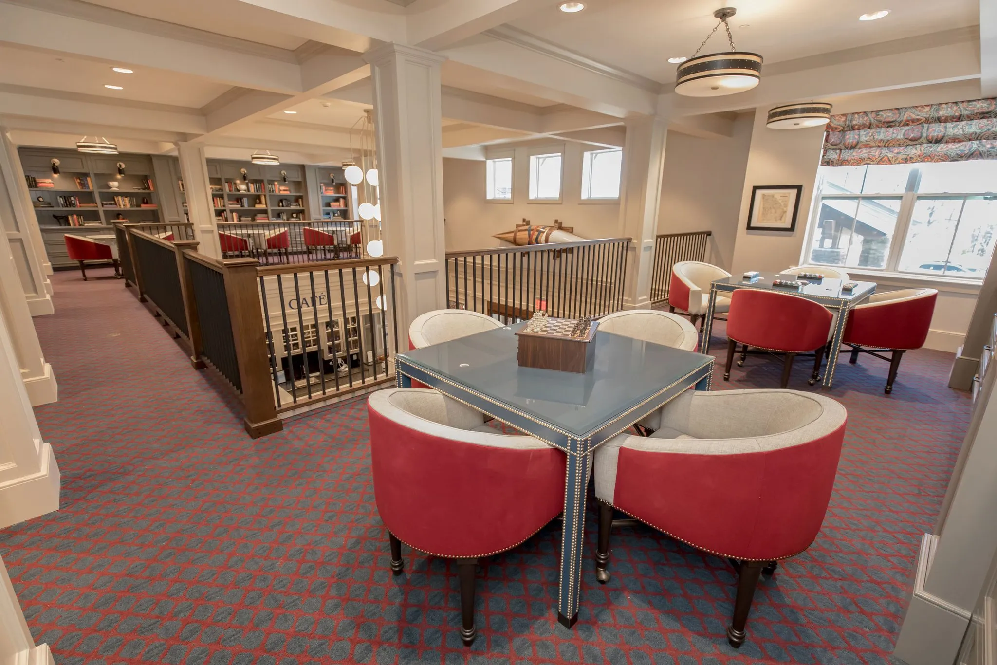 Senior living upstairs game room with red barrel chairs at a glass card table beside the wine racks
