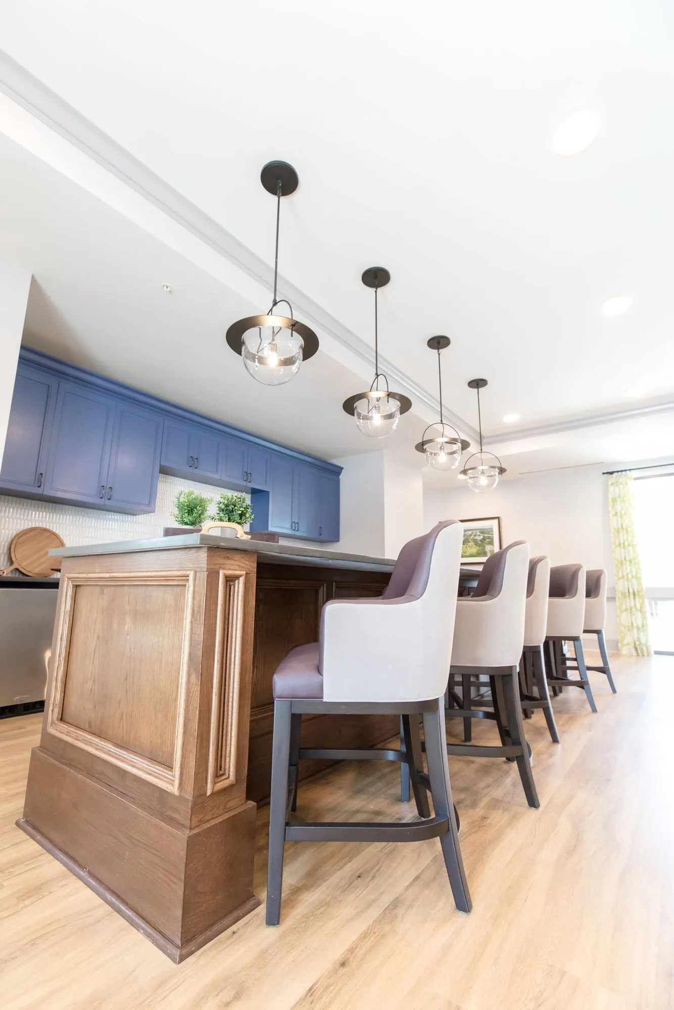 Senior living kitchen with the wood panelled island and grey counter stools, blue cabinets and a curtained window beyond