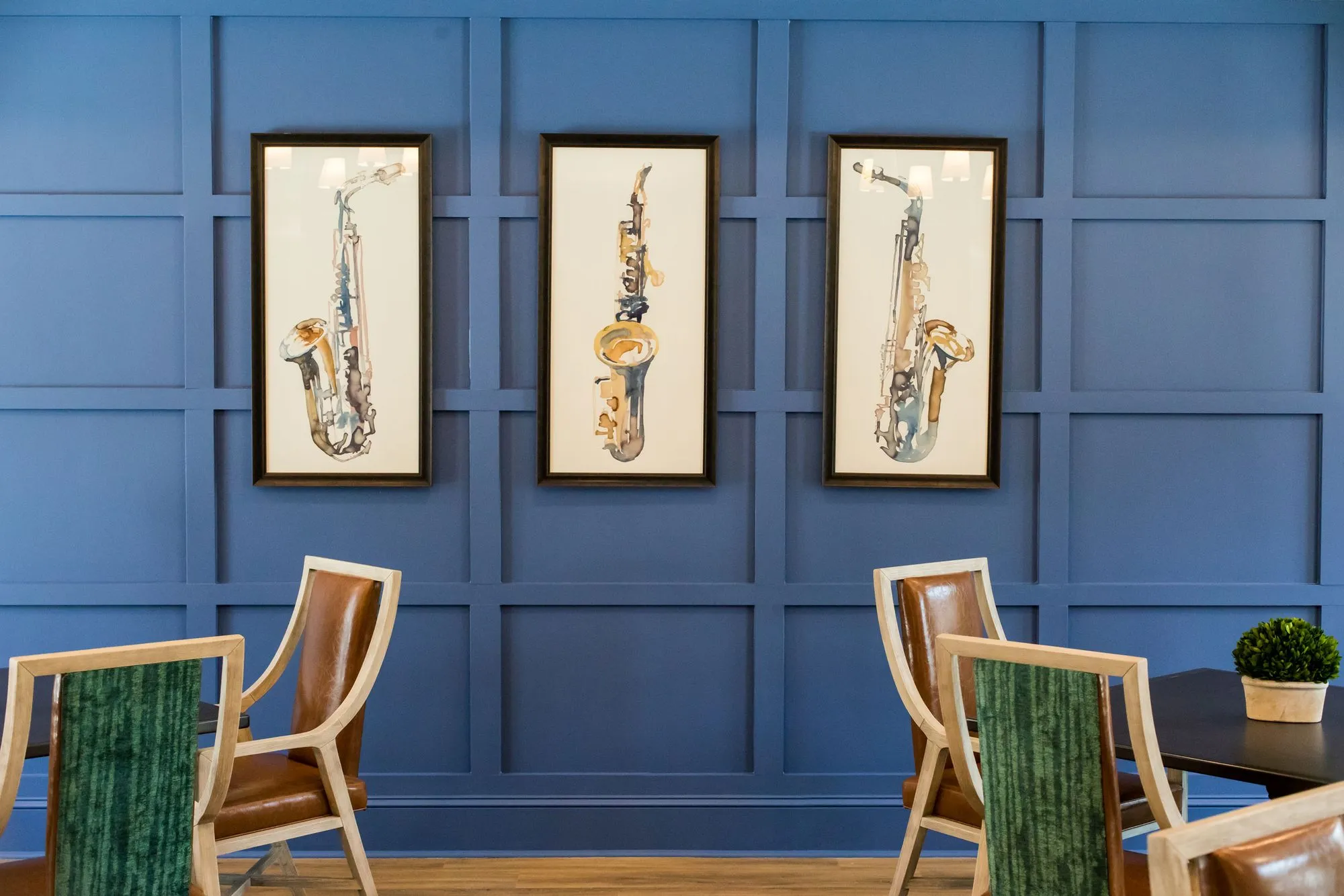 Senior living activity room with three framed saxophone prints on royal blue panelling above leather and green velvet chairs