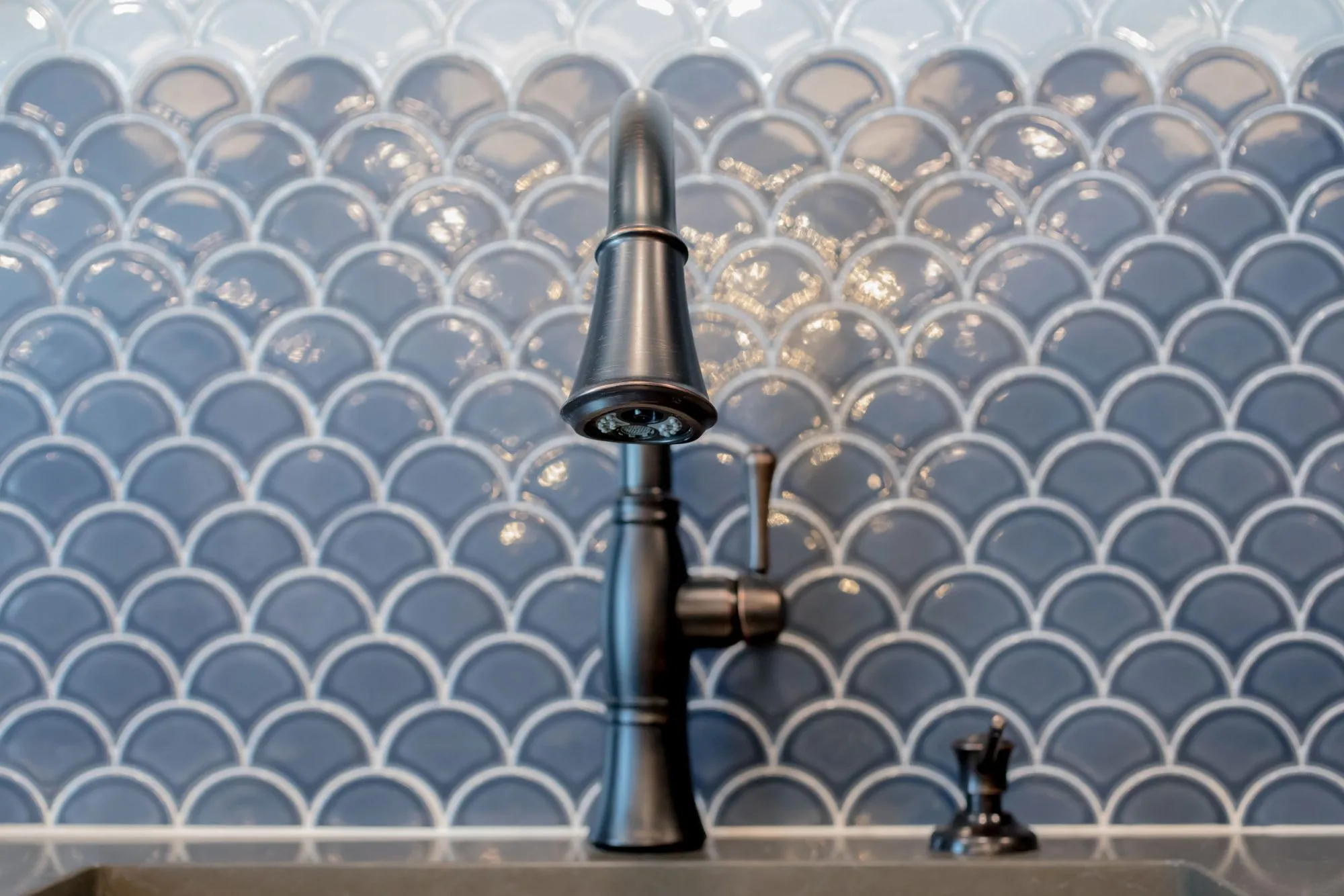 Senior living interior detail: black gooseneck faucet against a glossy blue-grey fish-scale tile backsplash