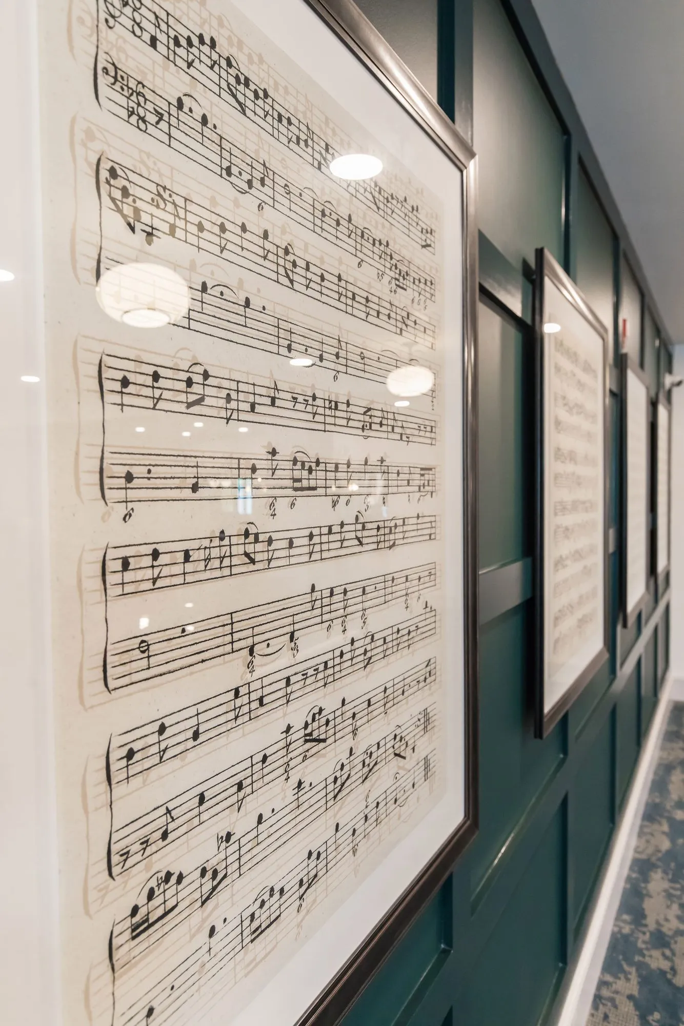 Senior living corridor with framed sheets of music hung along dark green panelling