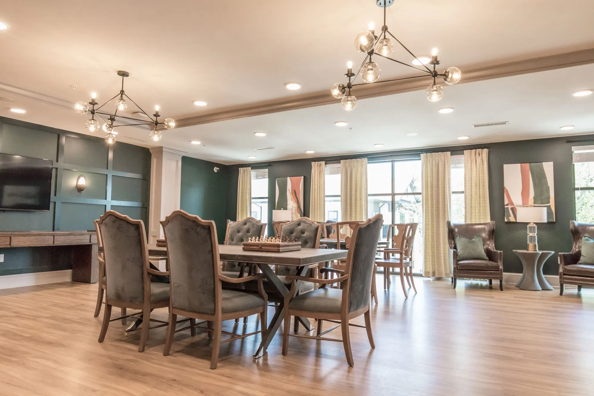 Senior living activity room with grey upholstered chairs around a chess table under brass sputnik chandeliers