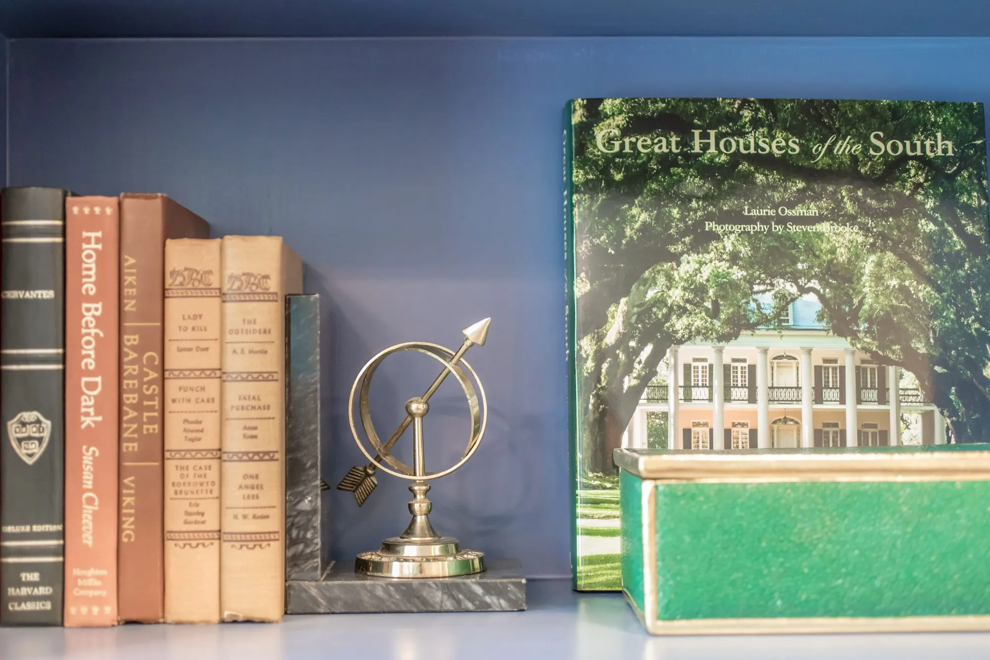 Senior living interior detail: old hardbacks, a brass armillary sphere and a coffee table book on a periwinkle shelf