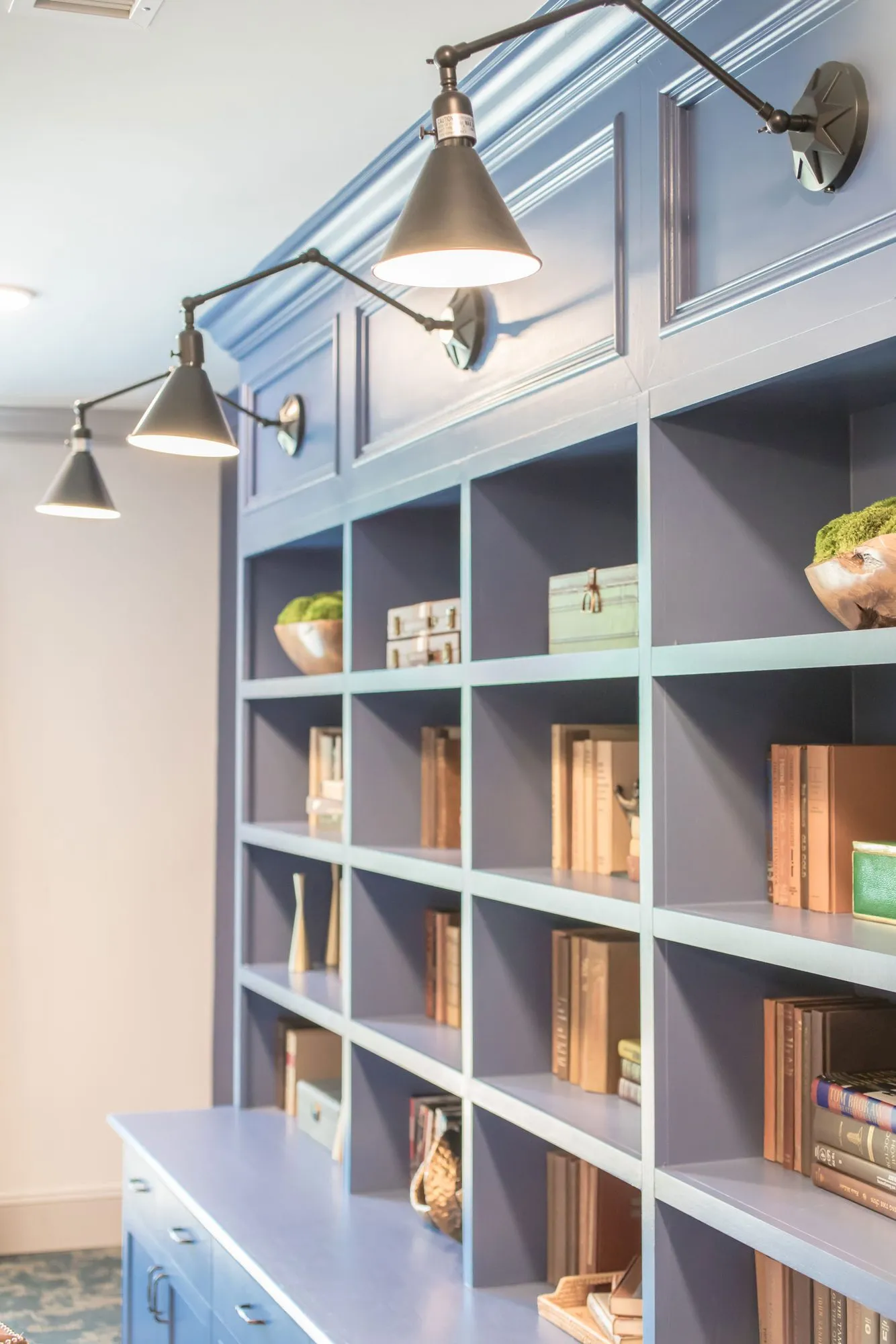 Senior living interior detail: periwinkle built-in bookcases lit by black swing-arm sconces, old books and wood bowls