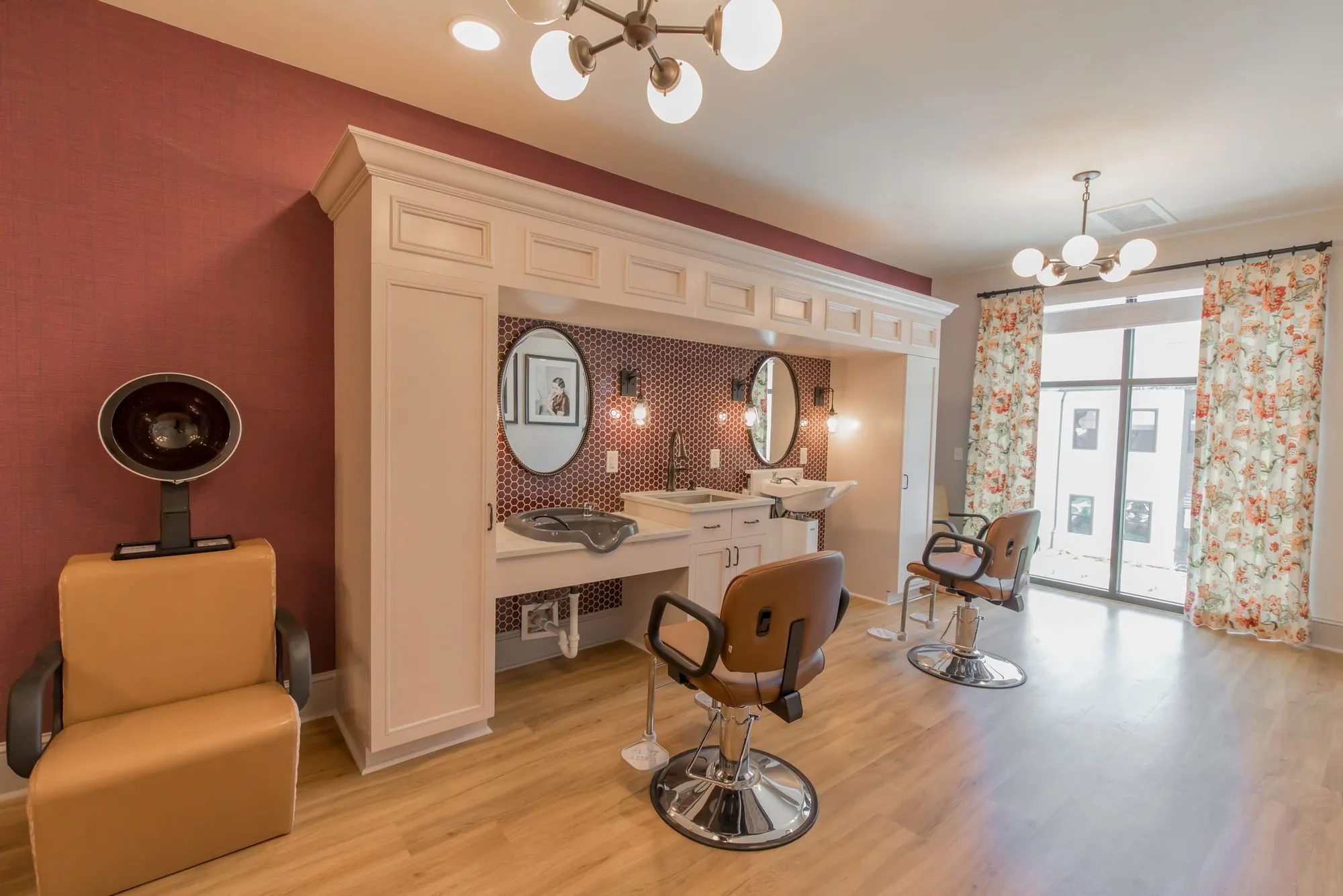 Senior living salon with a hood dryer chair, two styling chairs and a white vanity with round mirrors on a raspberry wall