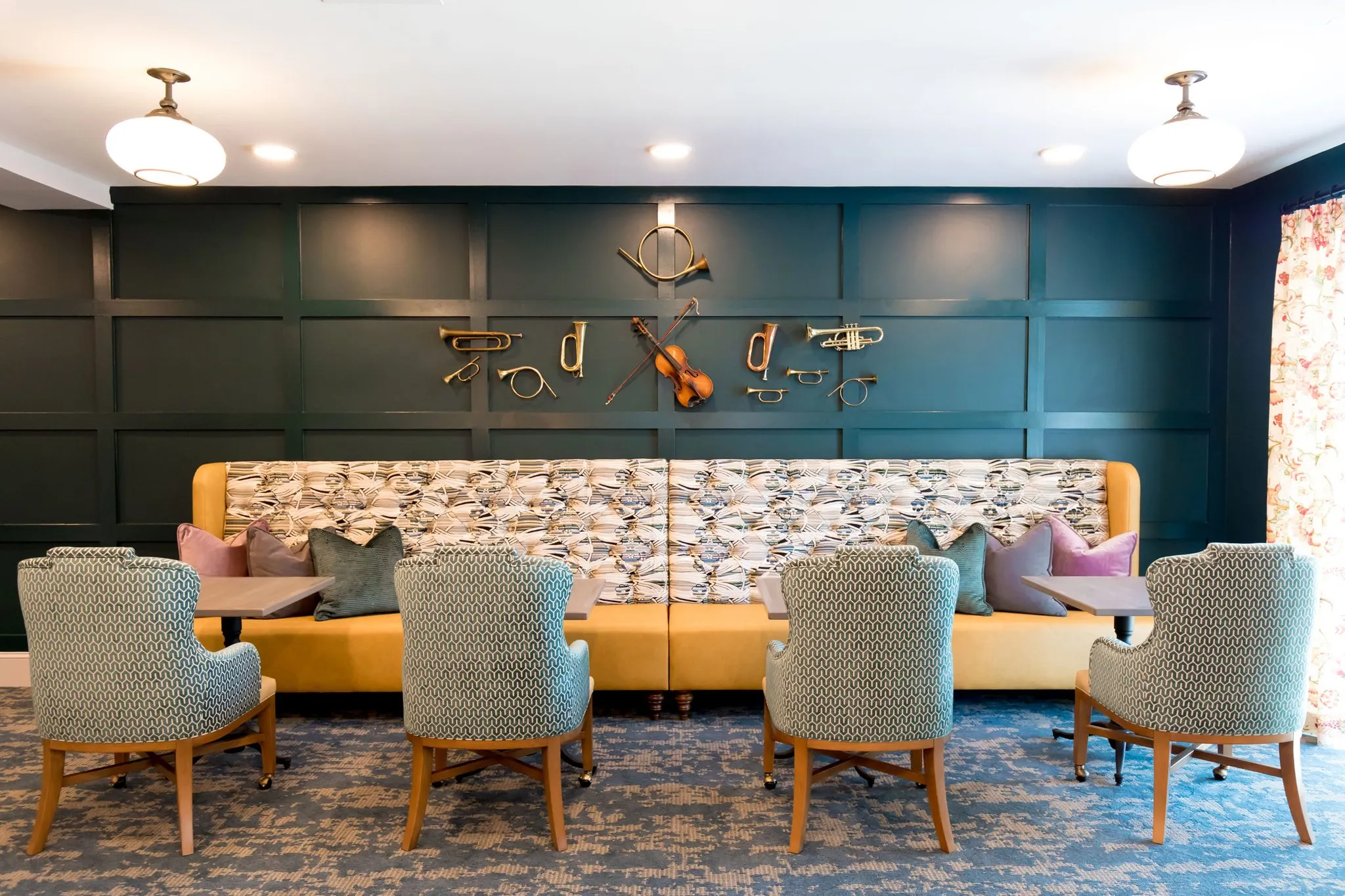 Senior living bistro with brass horns and a violin mounted across the teal panelled wall above a mustard banquette
